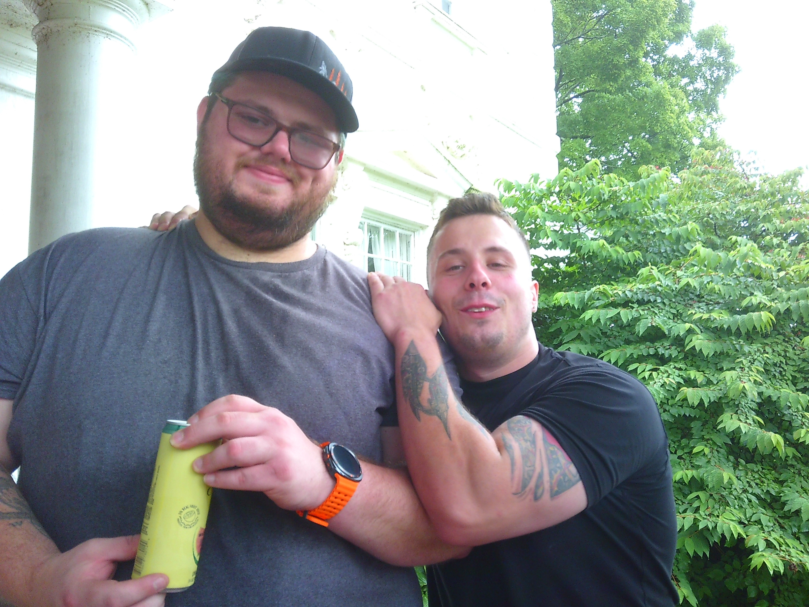 Photo of two men where one is holding a yellow canned beverage, and the other has both his hands on the first ones shoulders