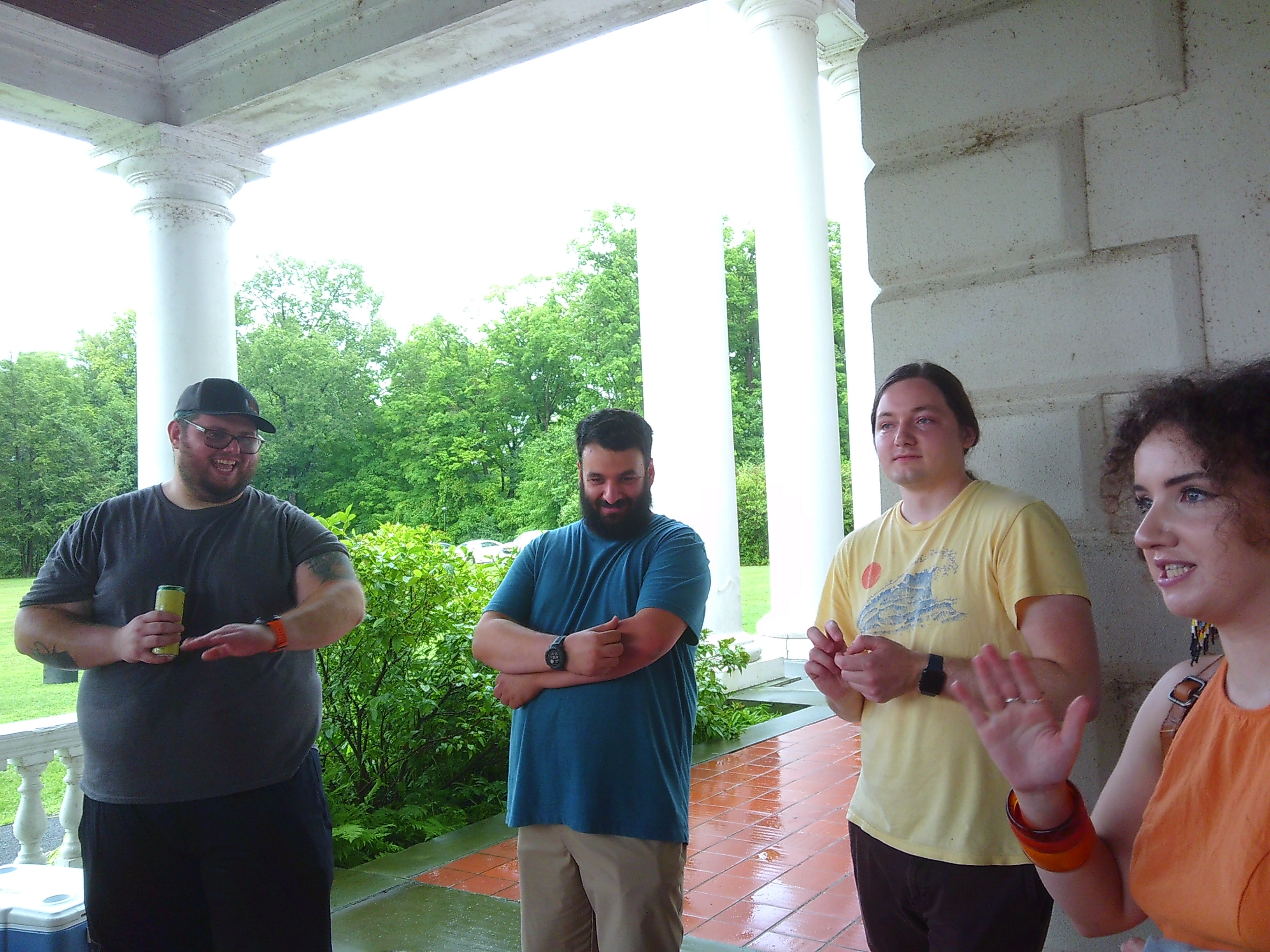 Photo of 4 people - a man in a grew shirt, a man in a blue shirt, a man in a yellow shirt, and a woman in an orange outfit. Both the grey shirtted man and orange wearing woman seem mid conversation.