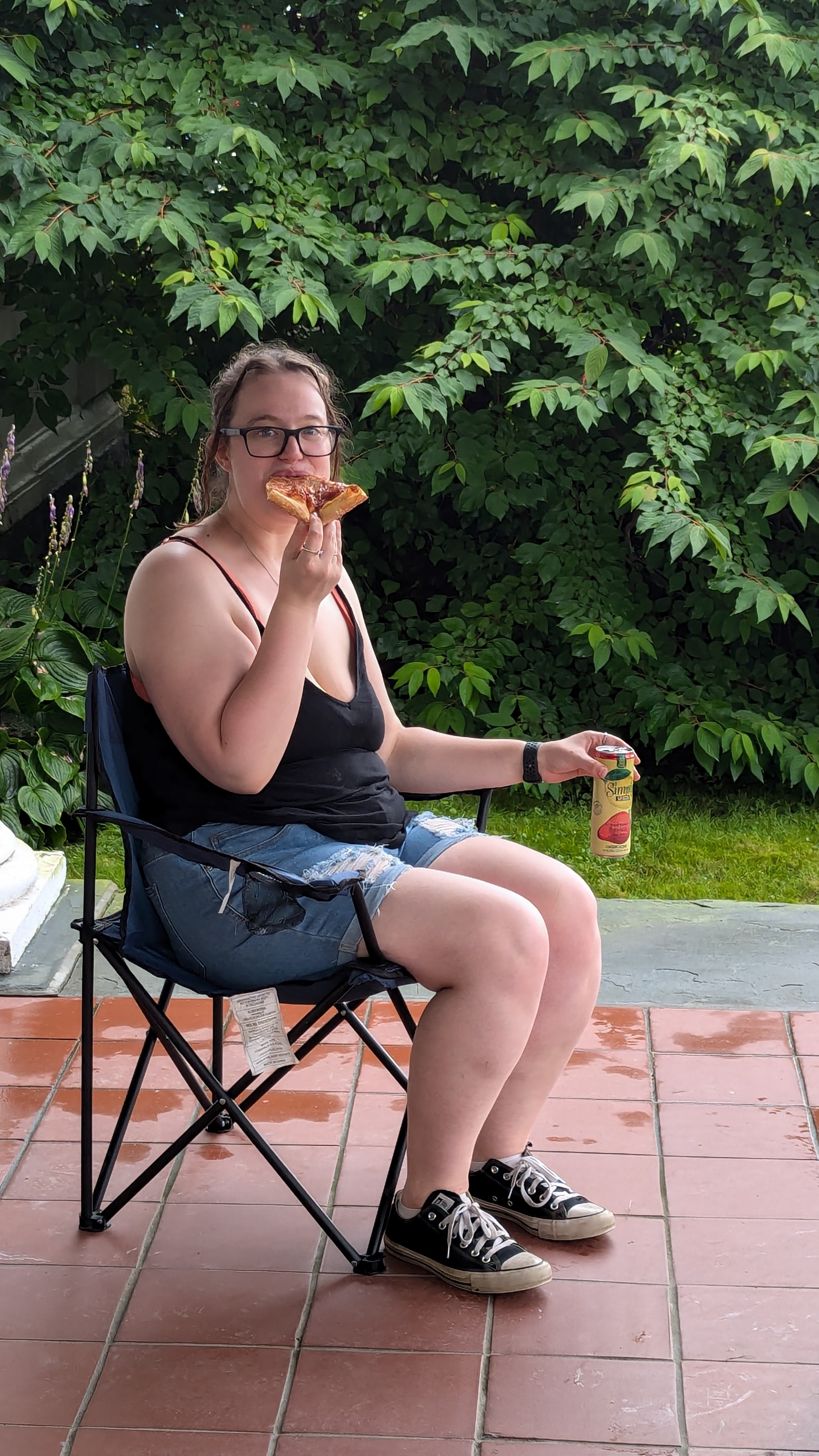 Photo of a woman sitting in a lawn chair eating some pizza