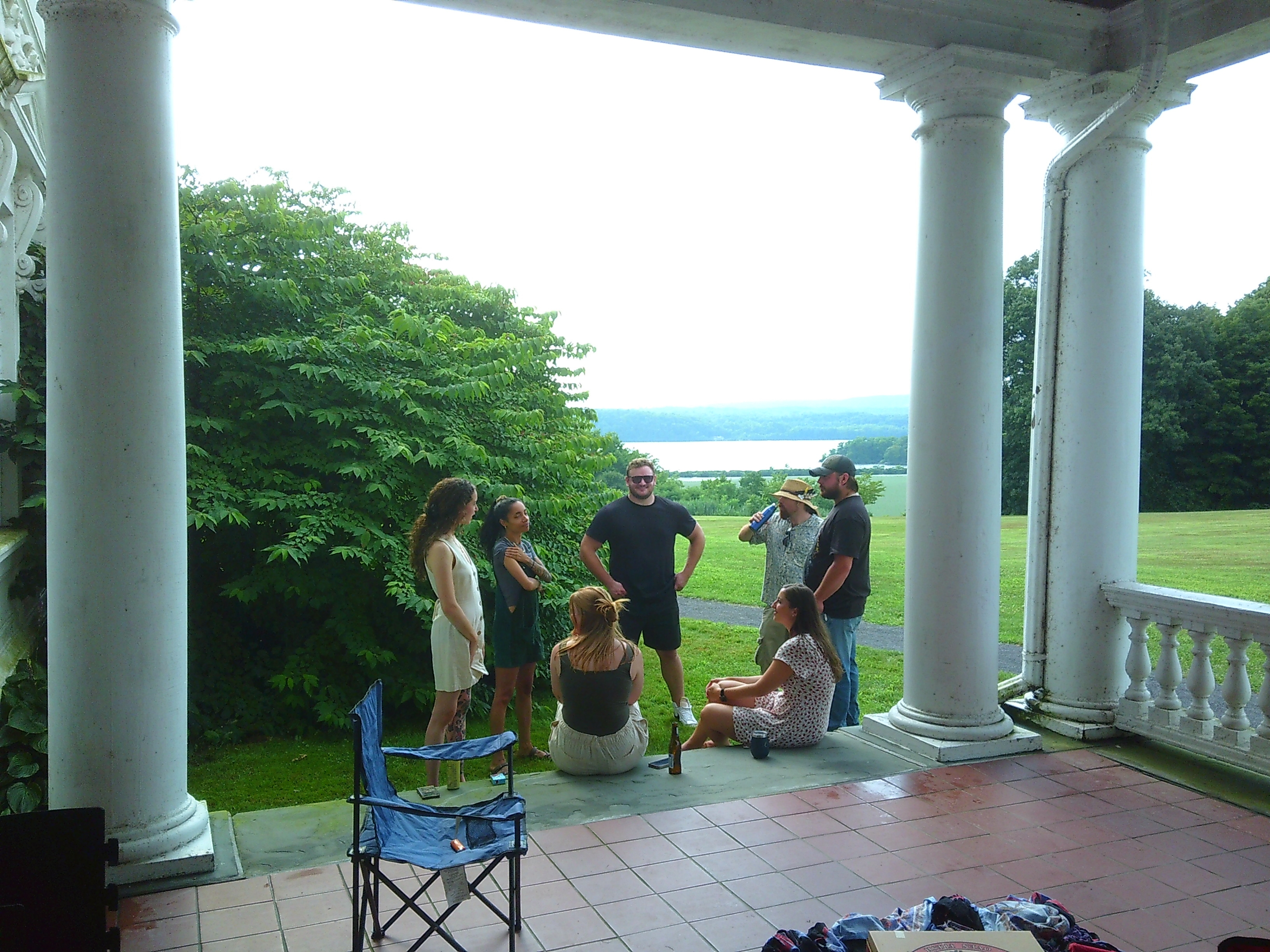 Photo of a group of people standing or sitting in a rough circle around some stairs with one person smiling directly at the camera