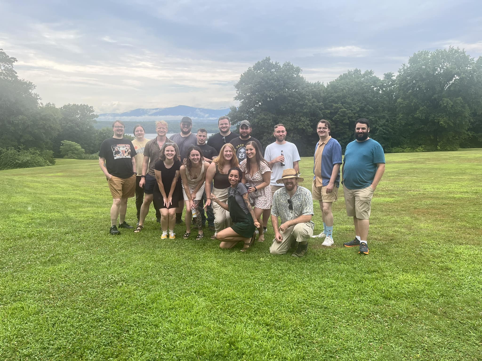 image of 16 people standing for a group photo on a lawn. In the background are trees, a river, and even a mountain in the distance. From left to right, starting with the back row, is Aiden Thomson, Sam Osterhoudt, Everett Knagg, Dane Mowris, Robert (Bobby) Morse, Travis Lasher, Todd Shanley, Patrick Martin, Dylan Thomson, Steven Tanzi. Middle Row, from Left to Right, is Mackensie Abela, Marissa Flannery, Daphne Schroeder, Colette Sofokles. Bottom Row from left to right: Ainsley Manino, Arlie Hart