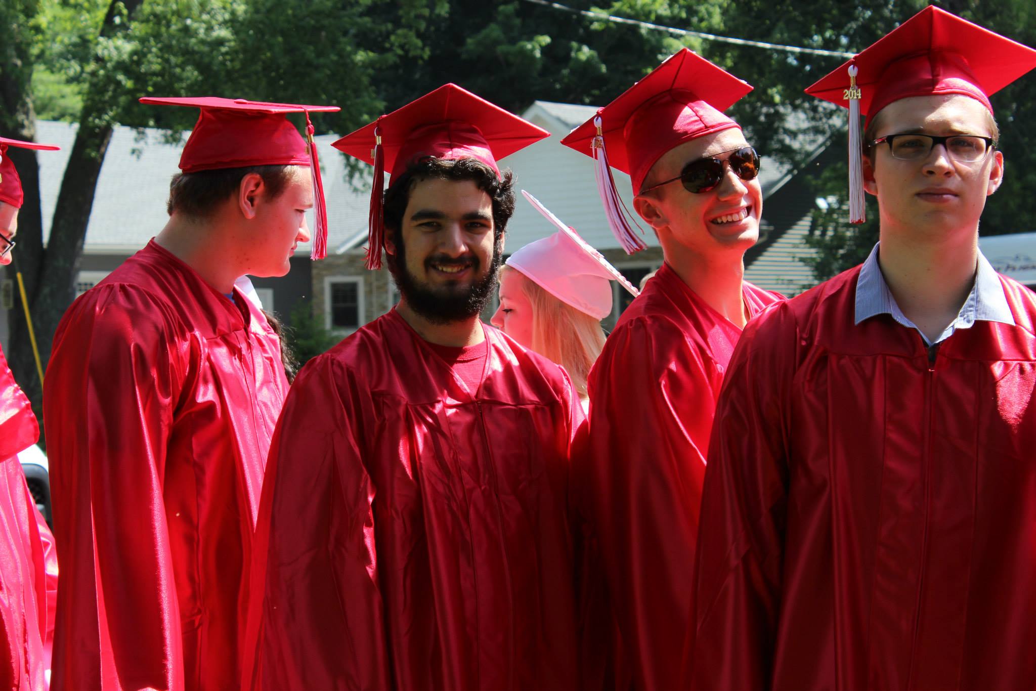 Photo of 4 high school graduating seniors outside in red robes and hats. From Left to right, Travis Lasher, Steven Tanzi, Nick Lombardo, Justin Timperio