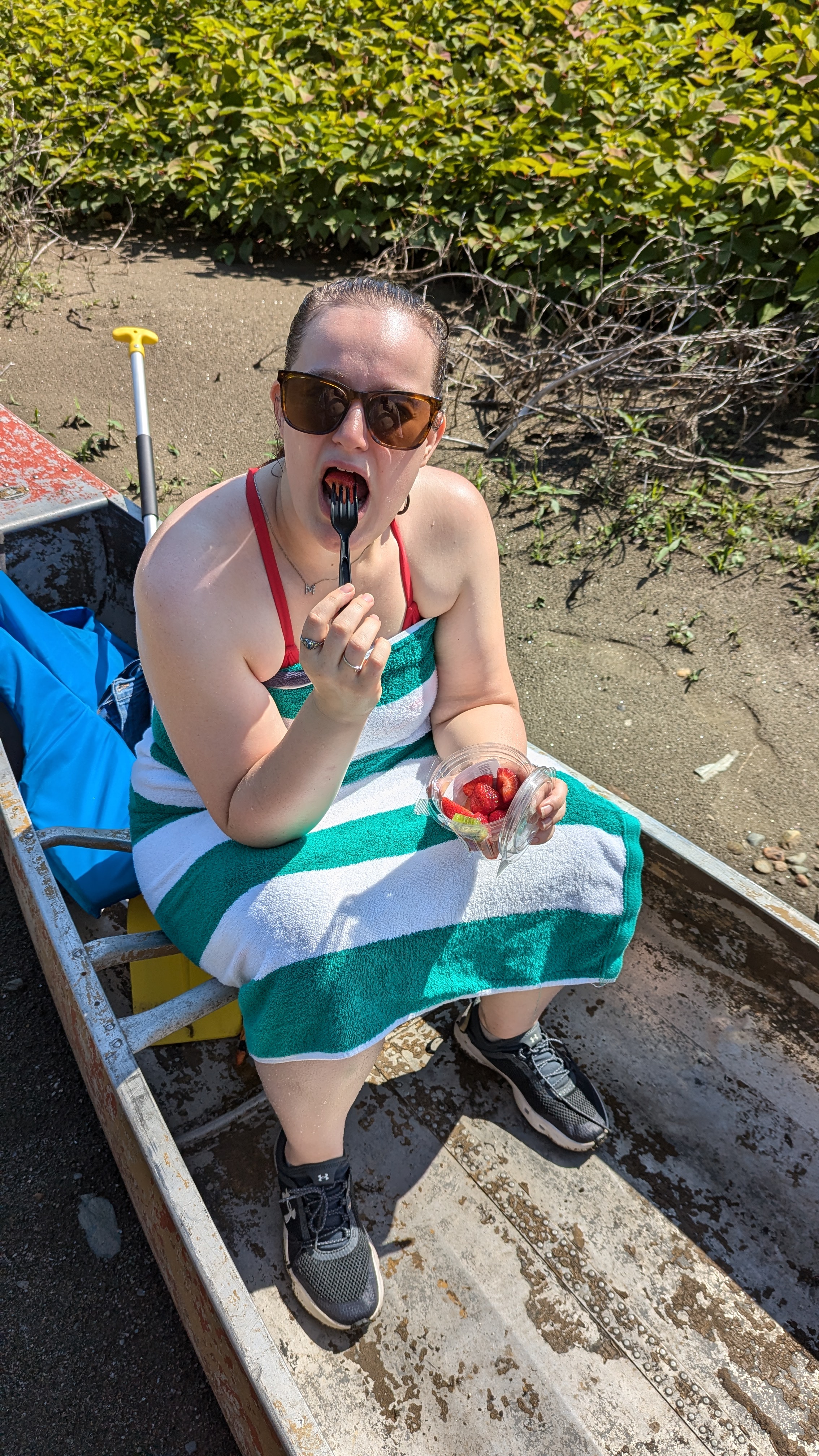 a photo of a woman sitting in a canoe eating strawberries. In this photo, she has just put the strawberry in her mouth