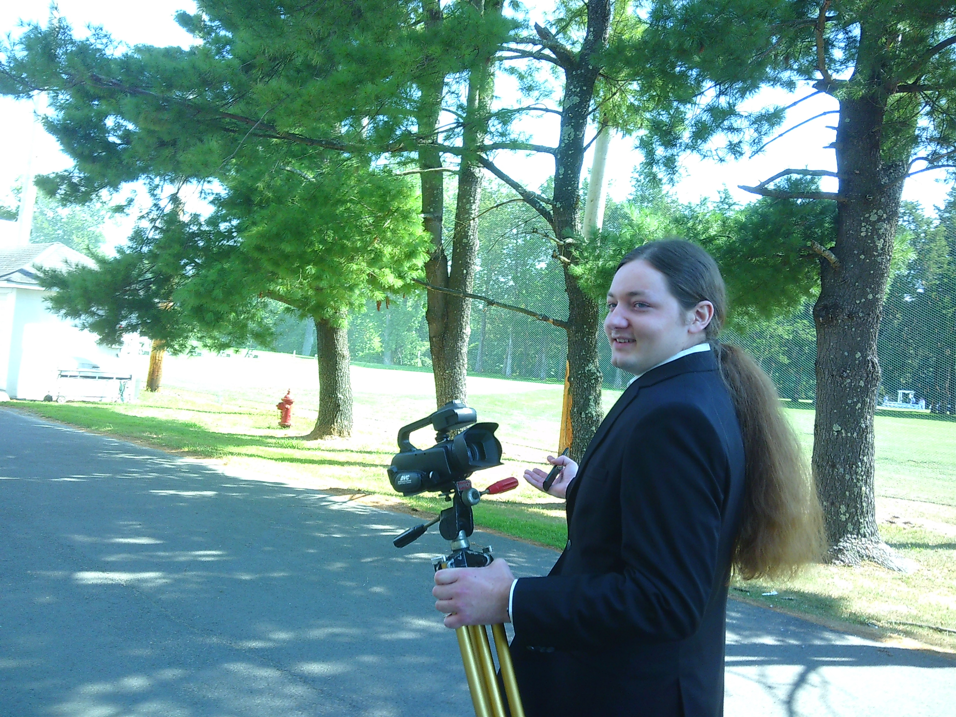 Photo of a man (The Groom, Sam) carrying a small camcorder on a tripod