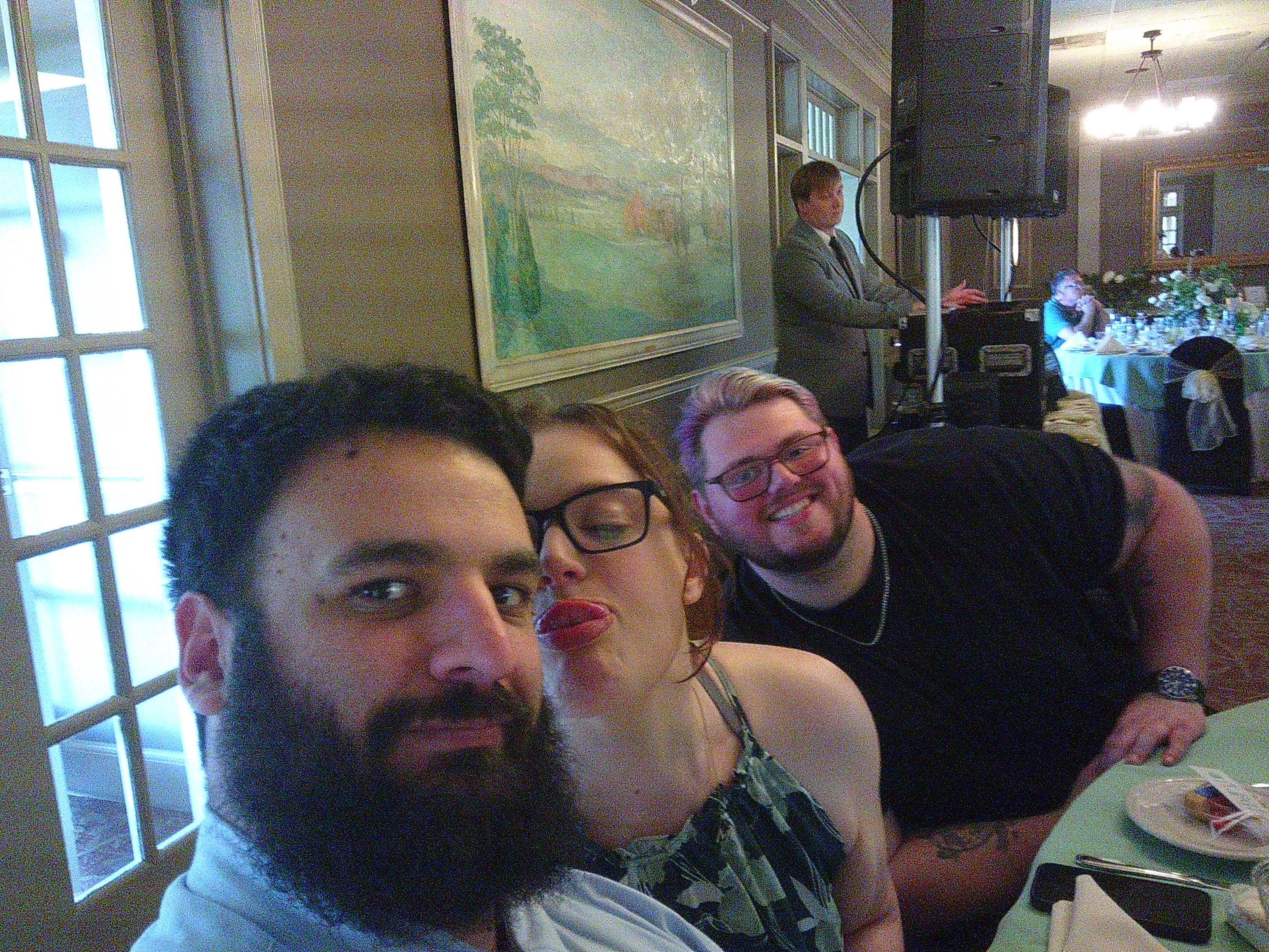 Photo of Me, Michelle, and our friend Dane at one of the tables inside during dinner. Michelle is sticking her tongue out towards me. The photo is taken as a selfie