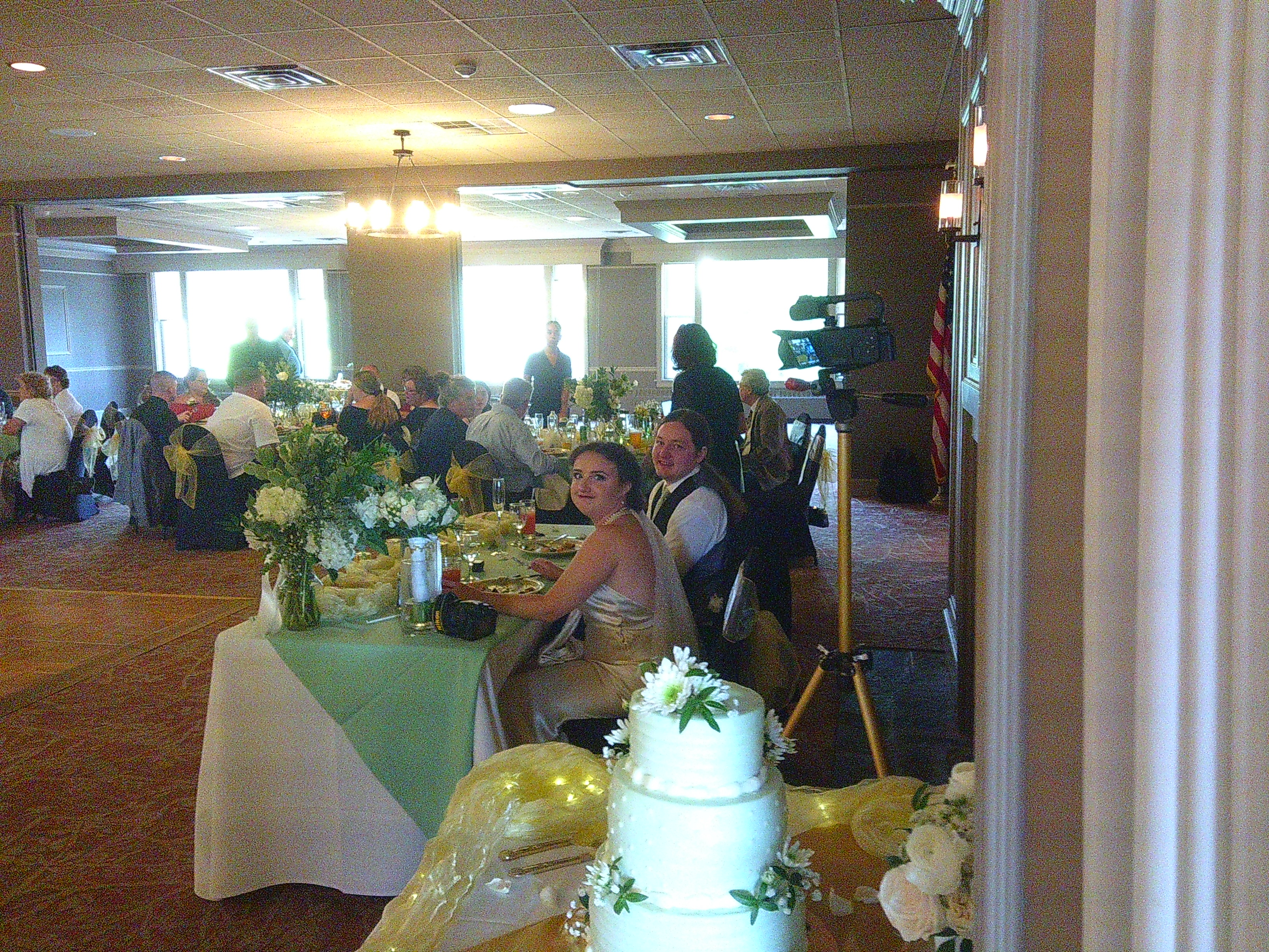 Photo of Sam and Zakiah (the Groom and Bride) at their table during dinner. Both are looking at the camera with Zakiah making a bit of a funny face