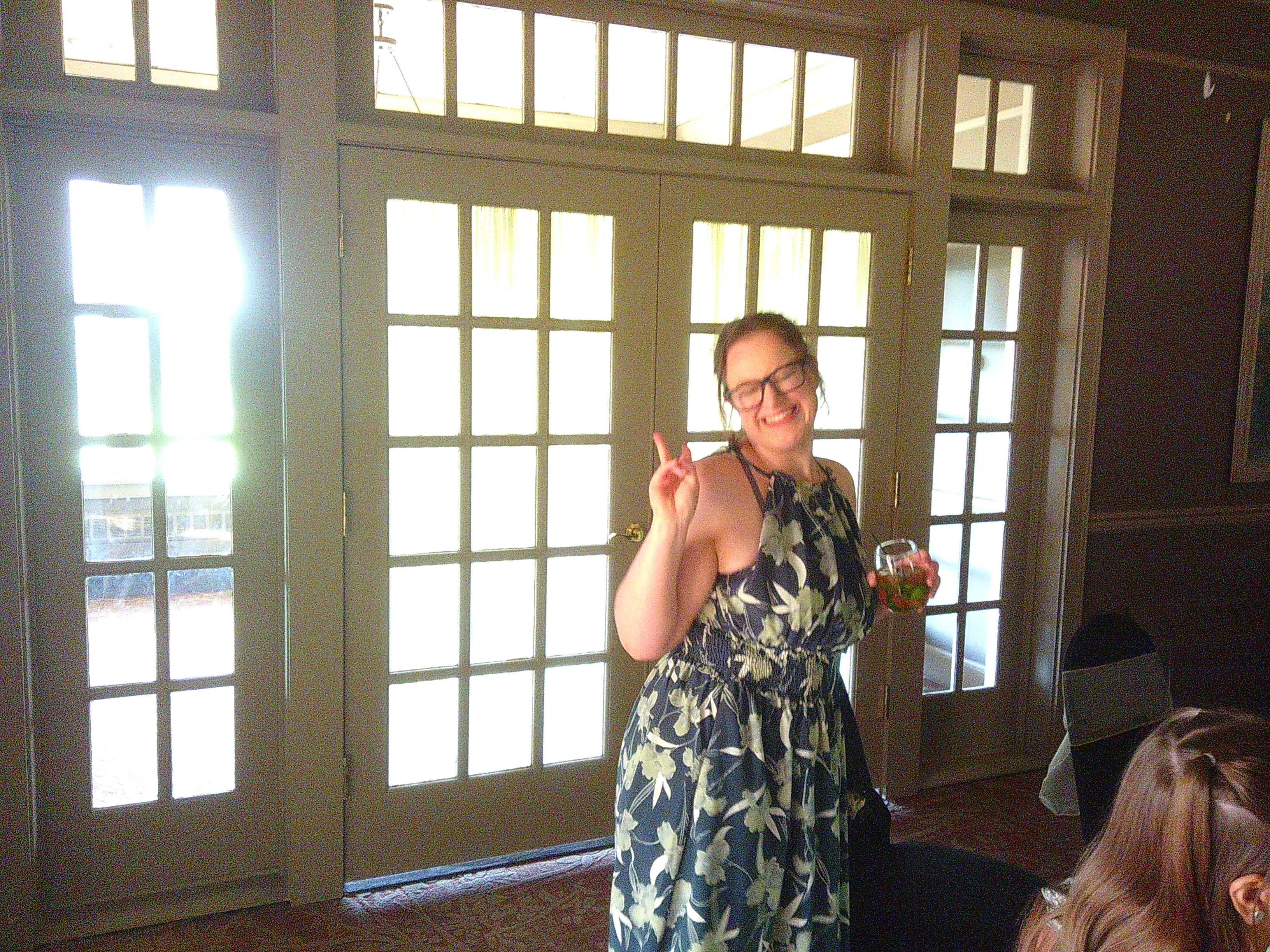 photo of Michelle giving the peace sign while inside. She has a cocktail in her other hand