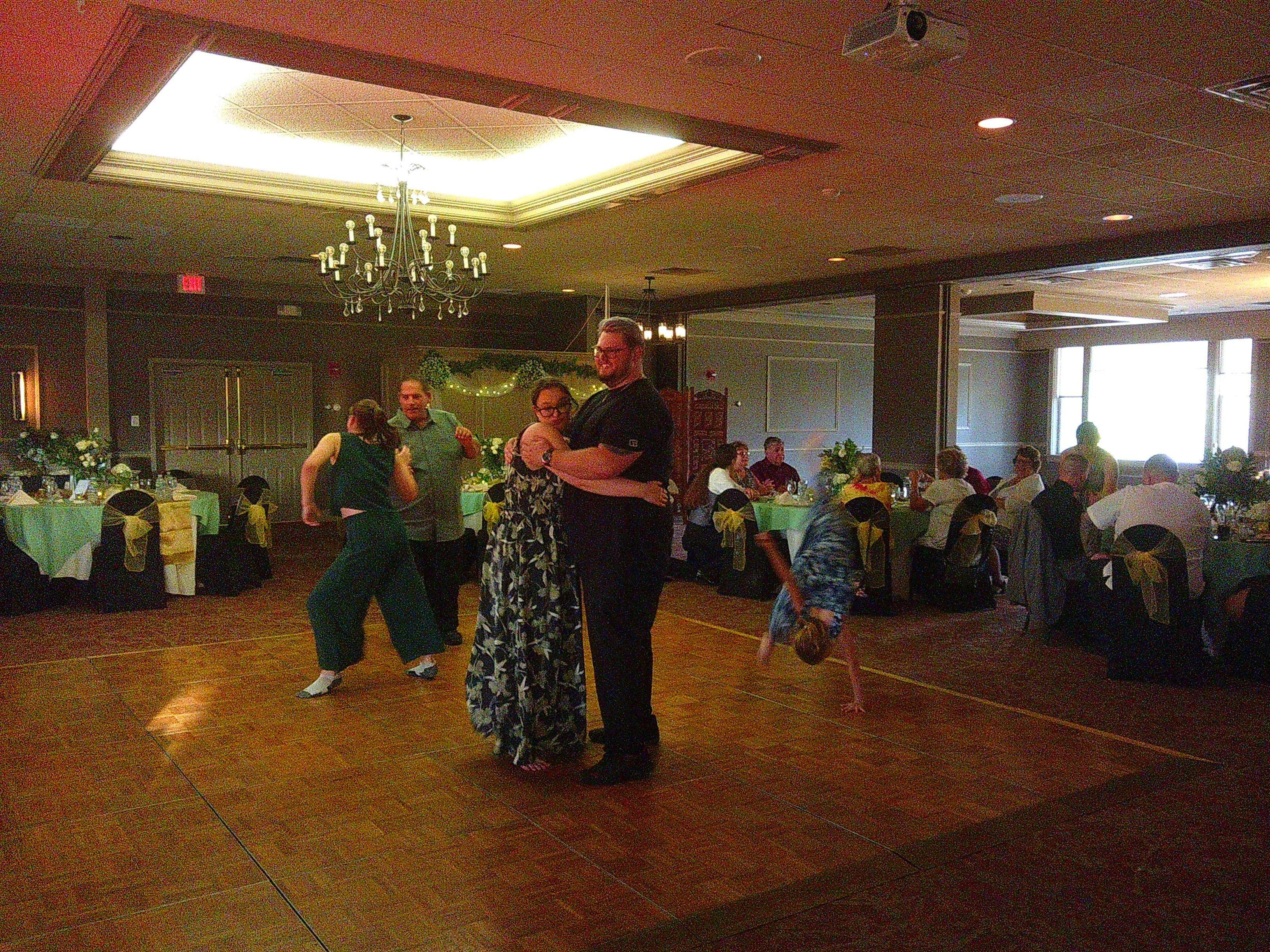 Photo of Michelle on the dance floor with Dane giving him a hug. There is another woman and man on the dance floor in the middle of dancing. Also, the girl who's about 7-10 years old is in the middle of a cartwheel