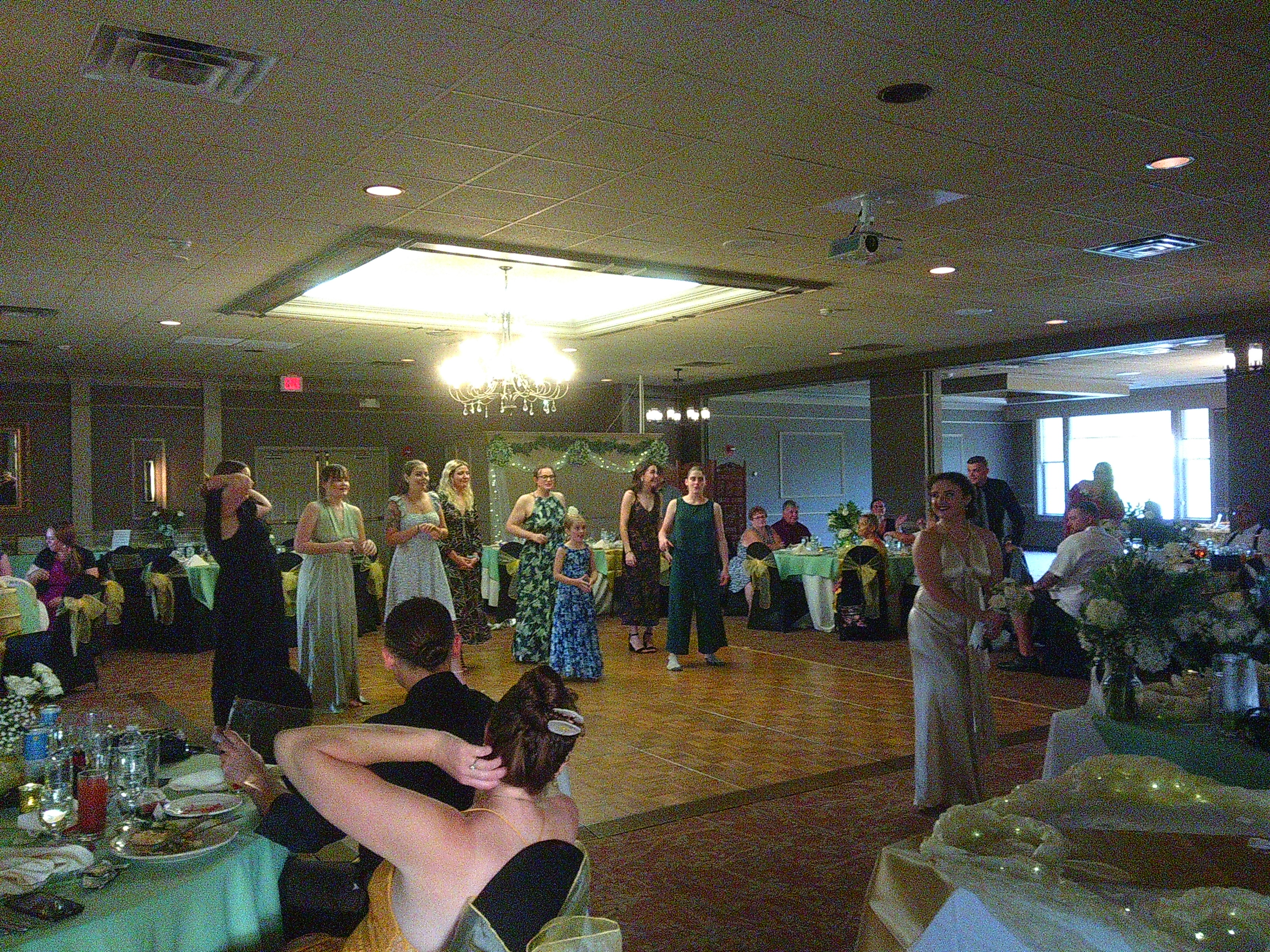 Photo of the bride, Zakiah, half looking behind her getting ready to toss her bouquet  of flowers. Behind her on the dance floor are all the unmarried women that were at the wedding