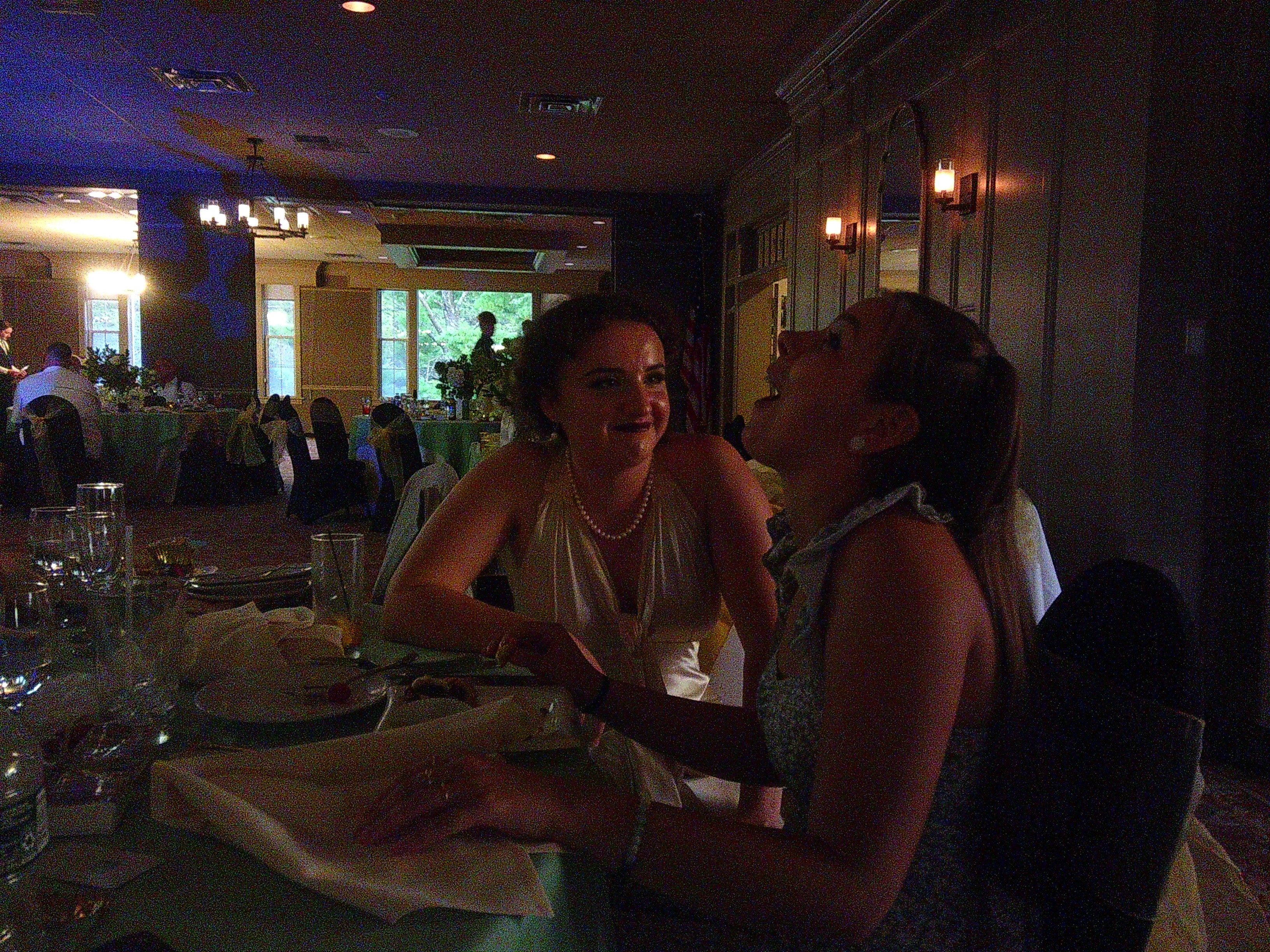 photo of the Bride (Zakiah) sitting down at a table next to another woman (Mercedes). Zakiah is smiling at Mercedes while Mercedes looks like she's mid laugh