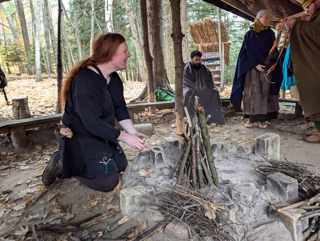 Photo of someone putting together a fire, with Steven wrapped in a grey blanket in the background looking off in the distance.