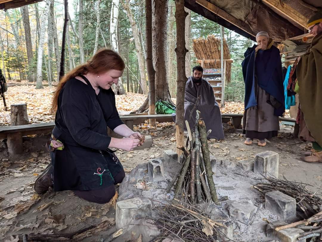 Photo of someone putting together a fire, with Steven wrapped in a grey blanket in the background looking towards the person putting the fire together.