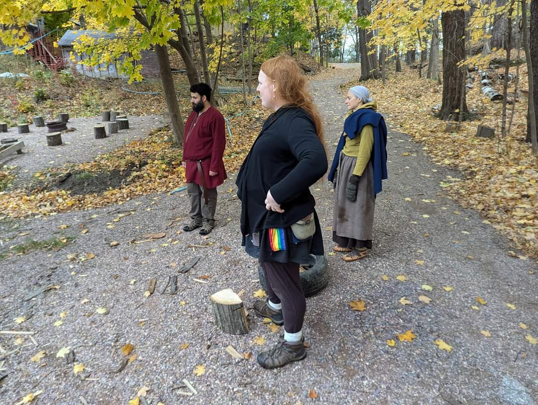 Group of peole standing on a dirt road, looking off to the left. Steven is in a red sort of robe with a belt tied around him.