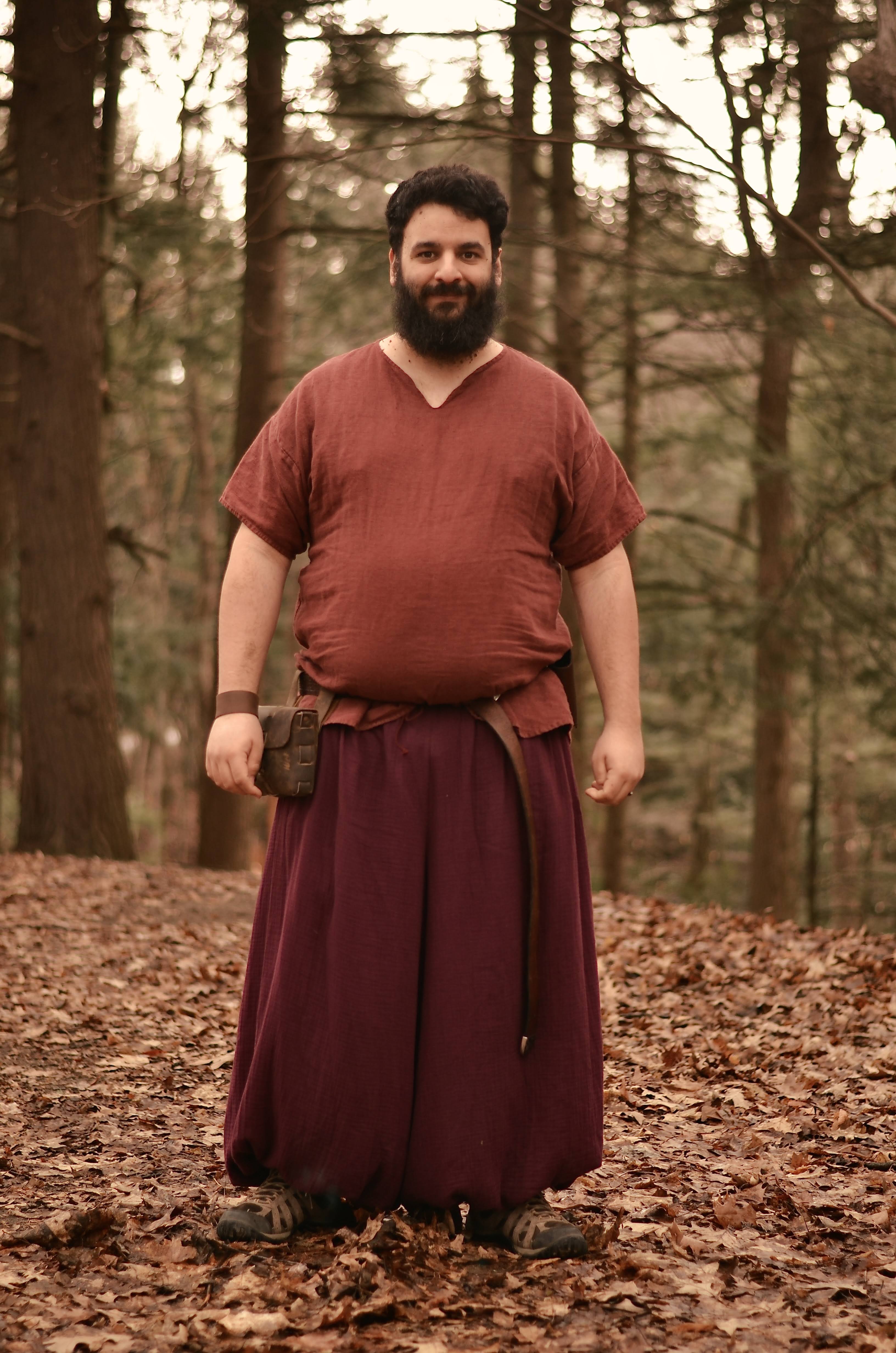 Photo of me, a bearded white man, in a red, v neck, medeival styled t-shirt, wearing a maroon pair of harem pants - poof sort of pants. You can also see a brown belt, with a pouch on my side, and a leather bracelet 