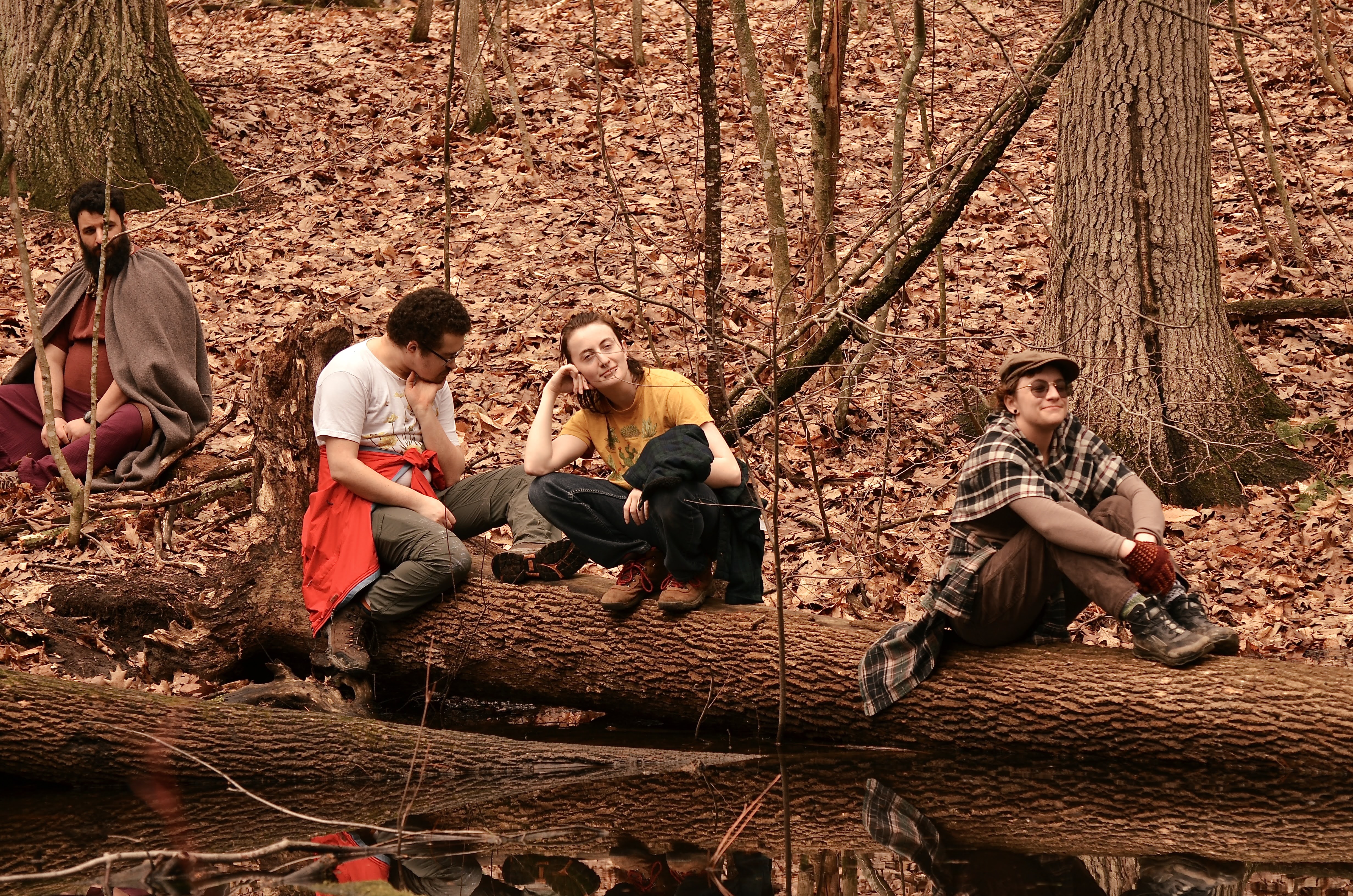 Photo of a few people sitting on a log over water, while I sit on the ground nearby