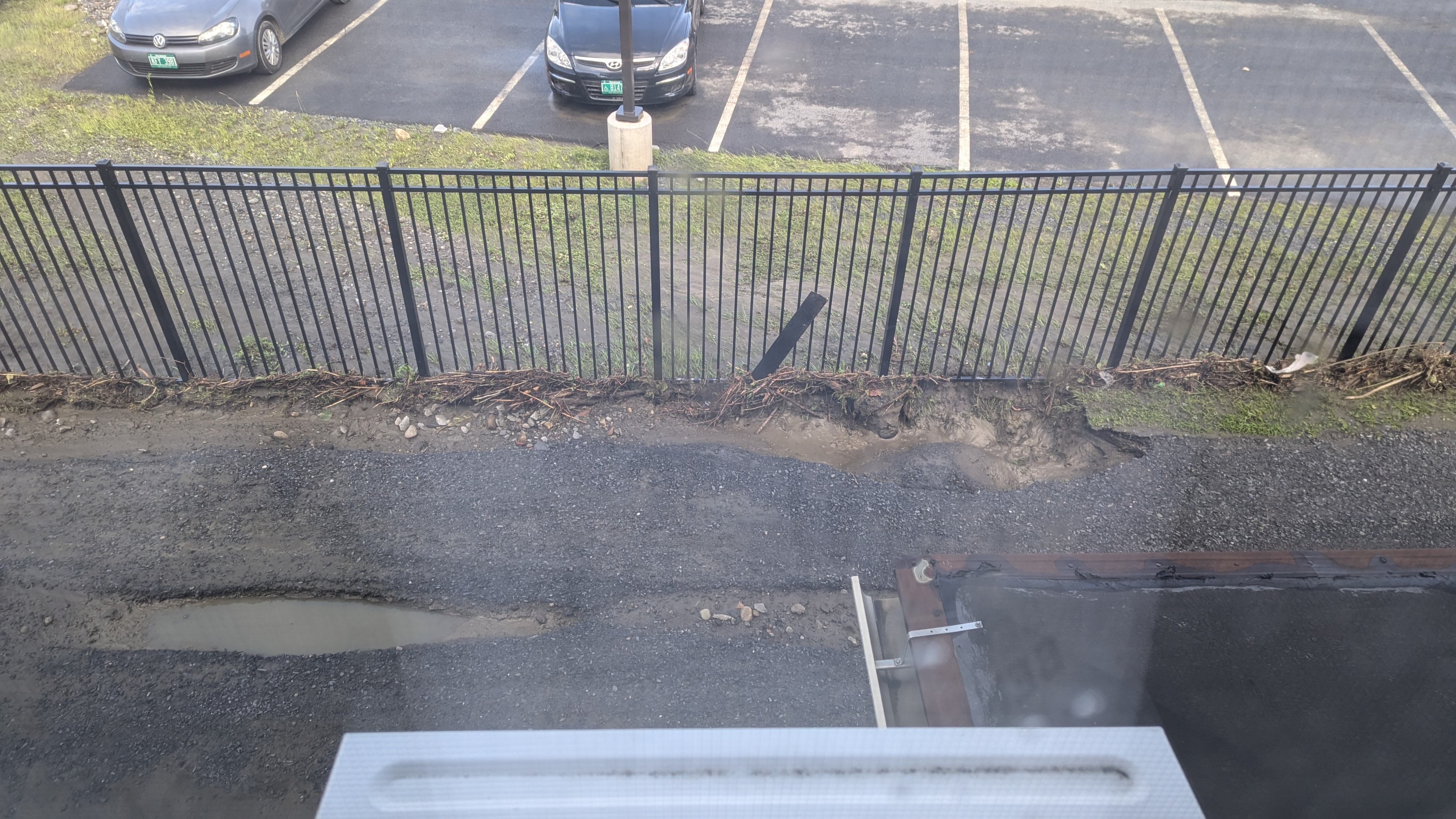 photo from out a window overlooking a driveway. Deep ruts can be seen in the dirt driveway, as well as a lot of debris washed up along a fence