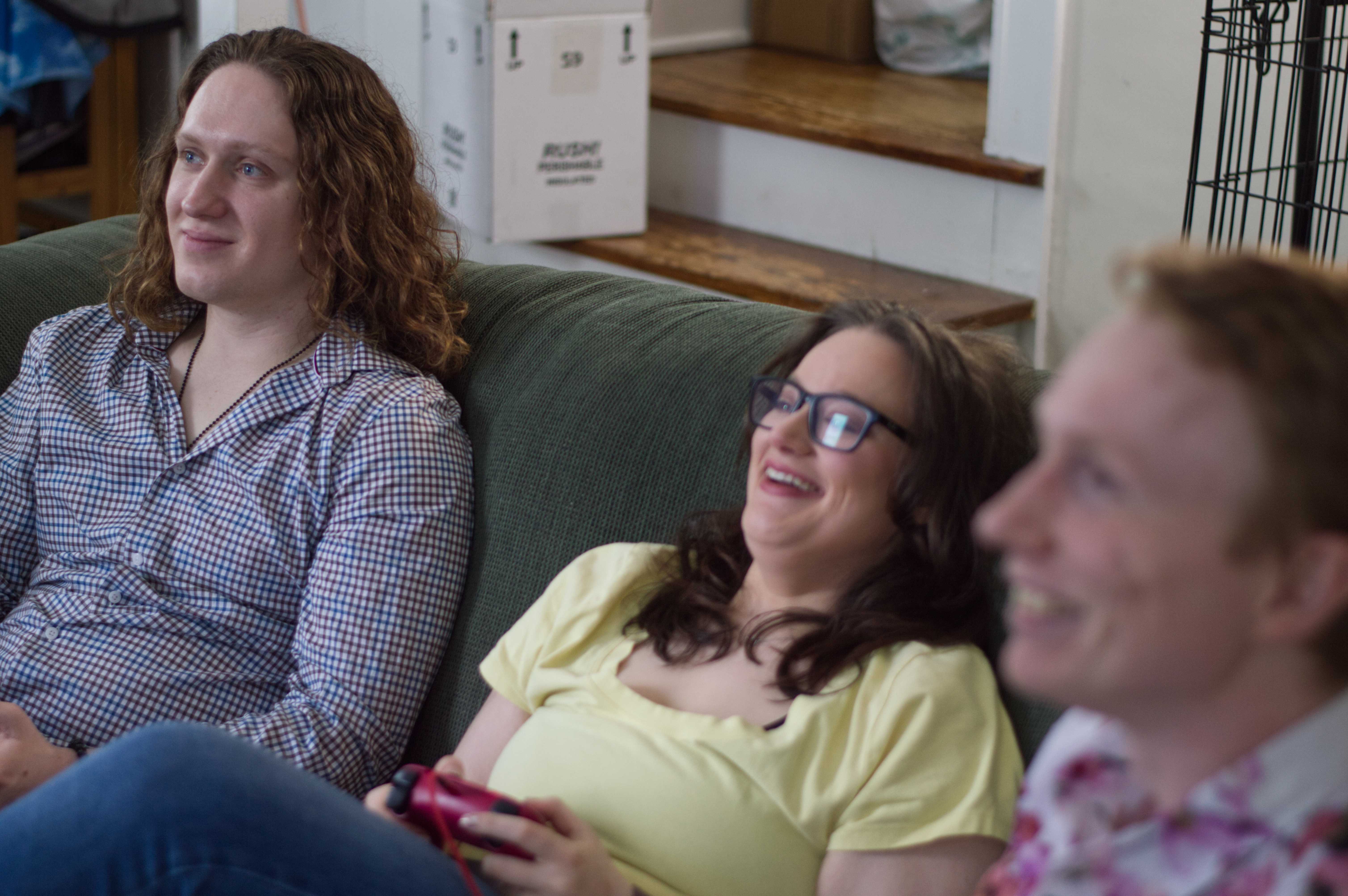 Photo of Josh, Michelle, and Mat on a couch playing a video game. They are all smiling, and you can see a Playstation 5 controller in Michelle's hands