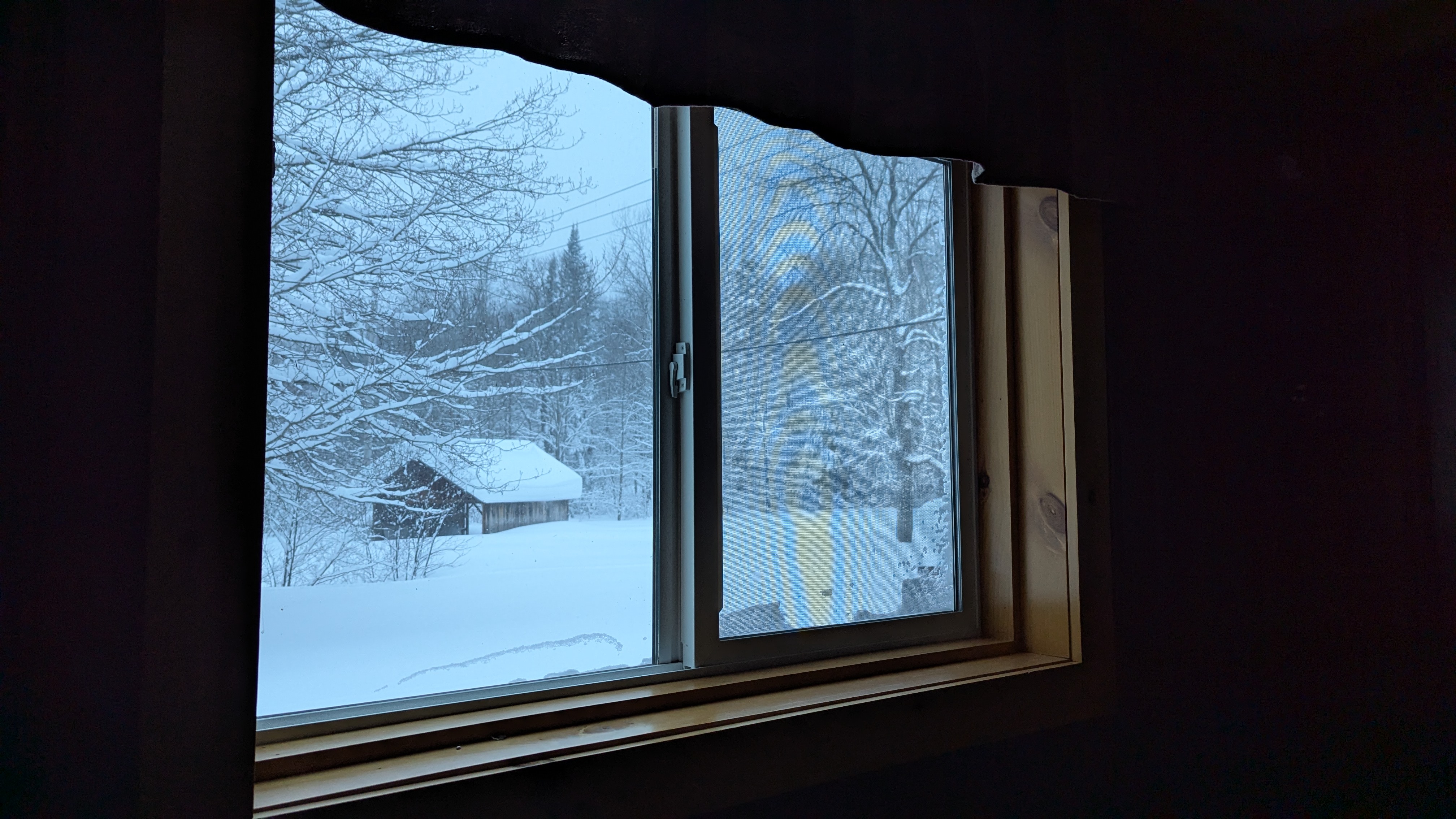 A photo of a snow covered landscape, looking at a covered bridge, from out a window inside of the Cabin