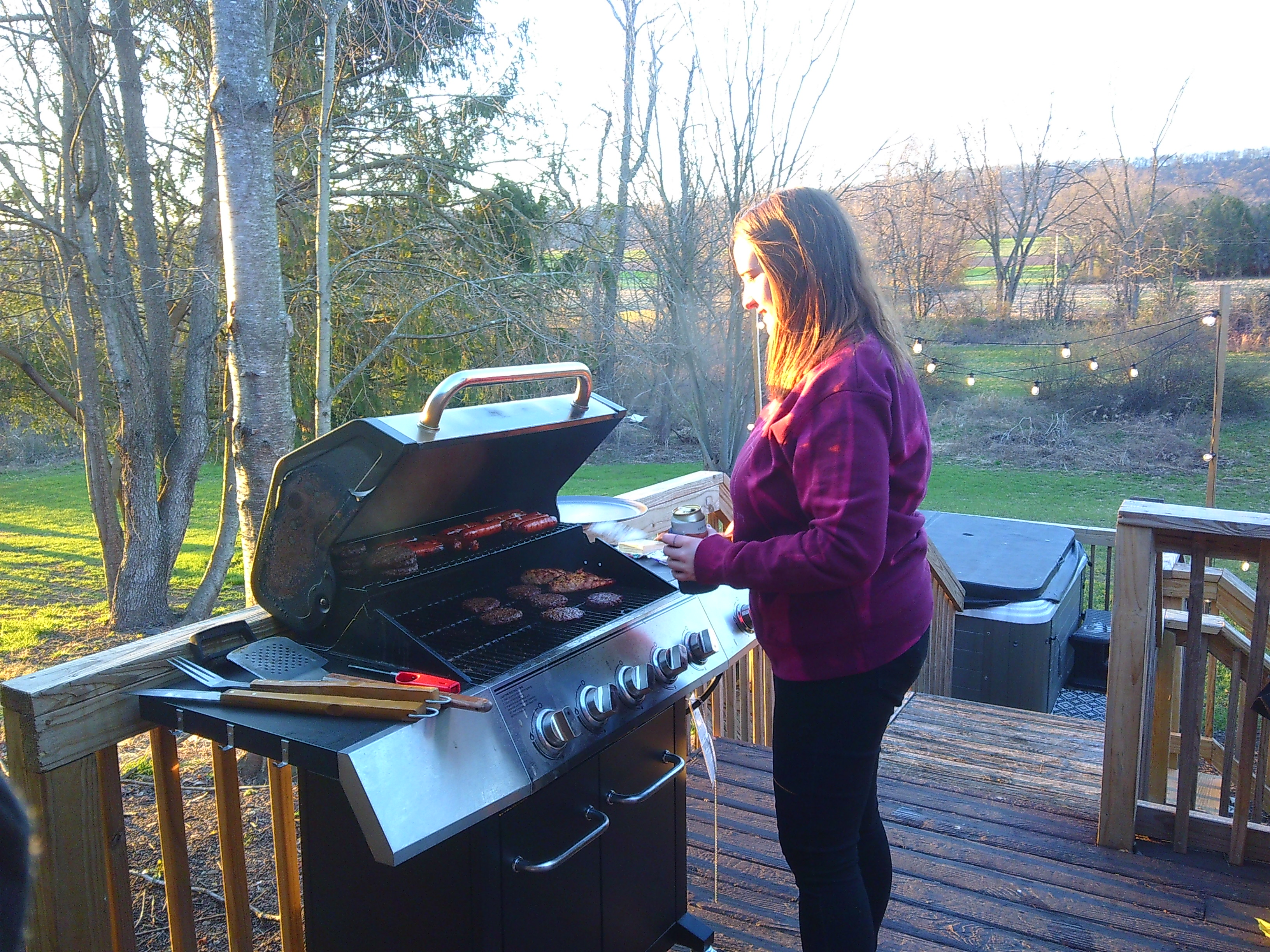 photo of a woman in a purple sweatshirt grilling burgers and hot dogs outside