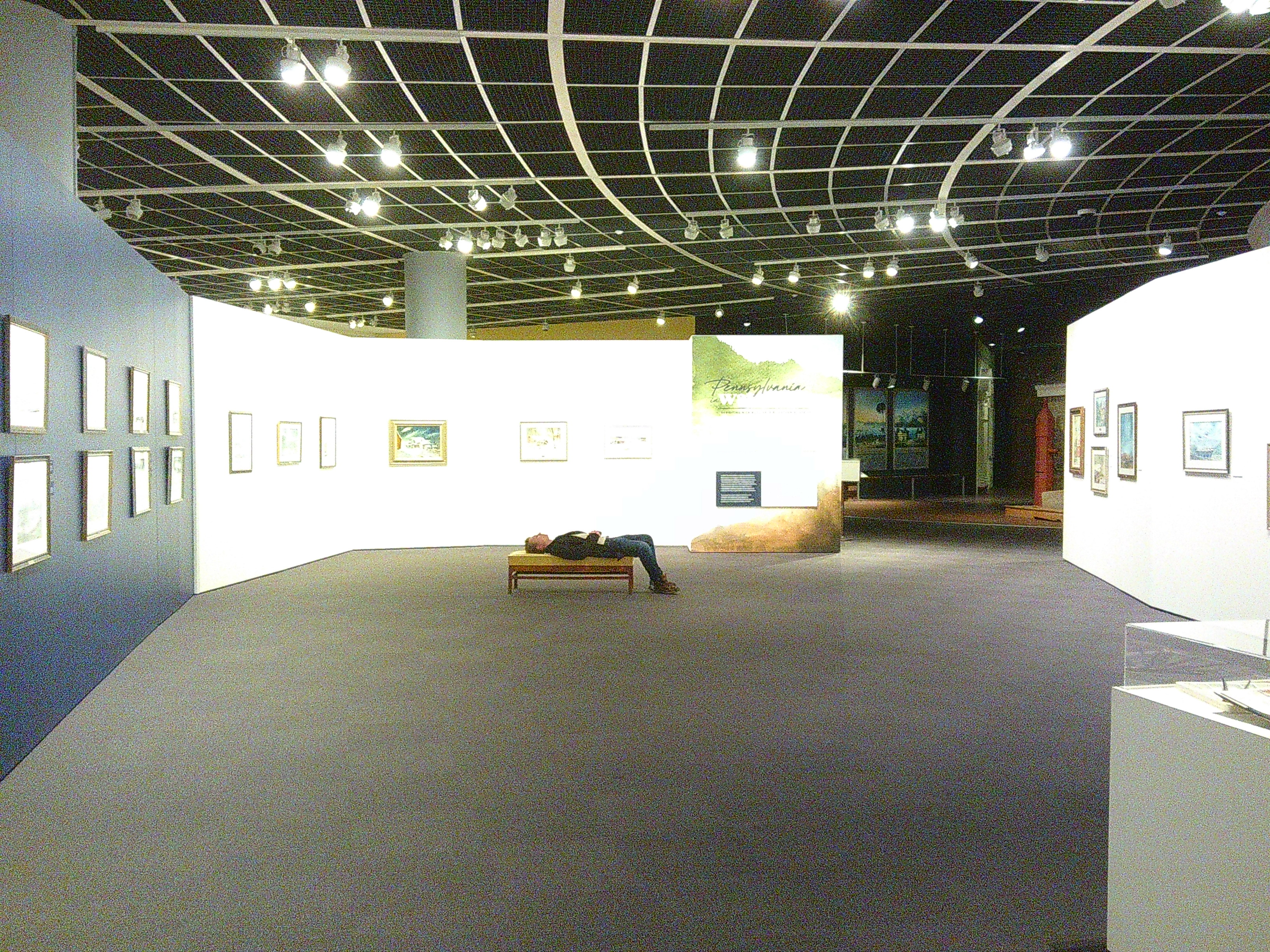 photo of a man in a museum, surrounded by art, laying down on a bench. It appears he's sleeping