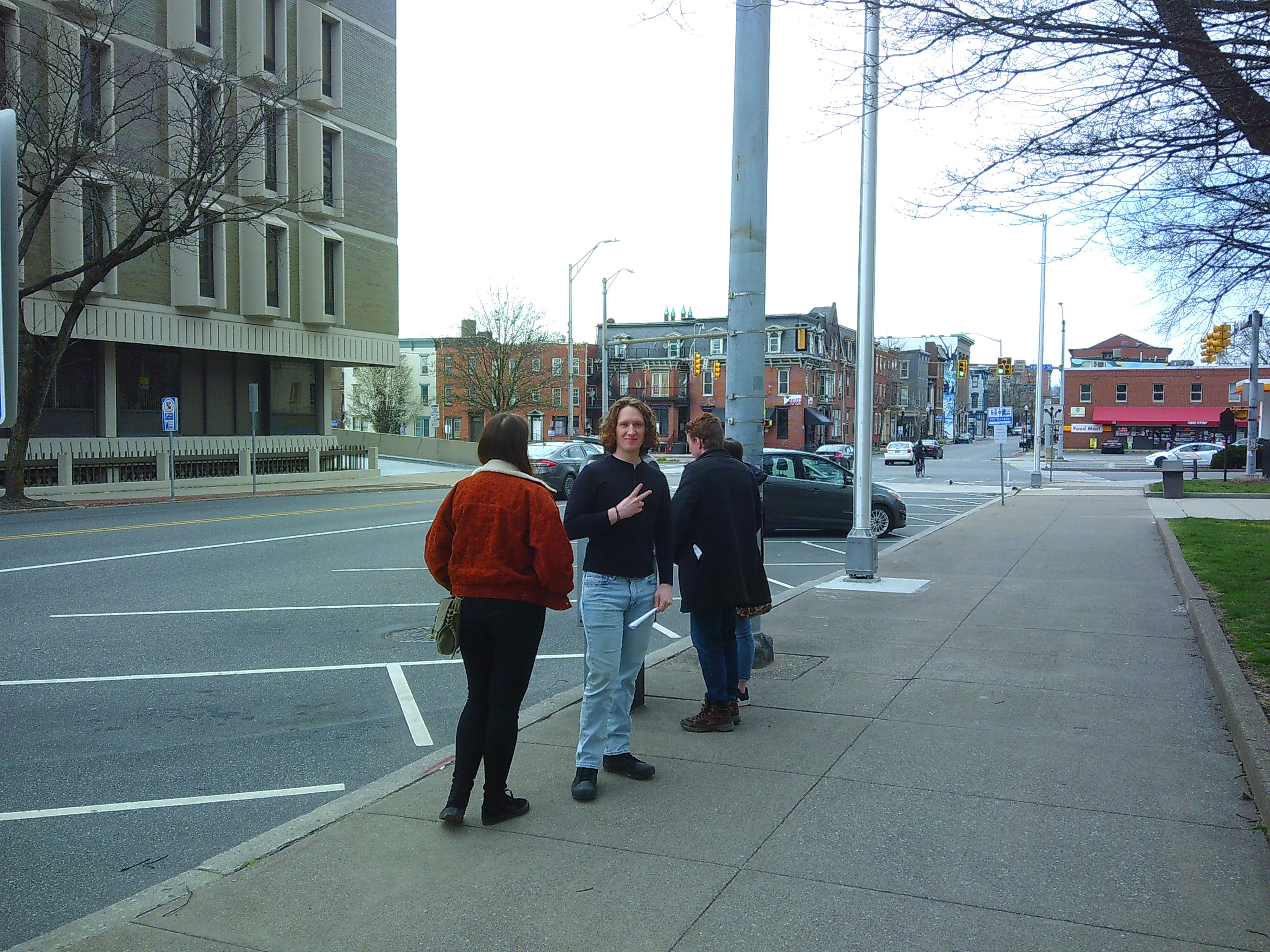 Picture of 4 people on the sidewalk on a street in Harrisburg Pennsylvania. One person is facing the camera holding a peace sign