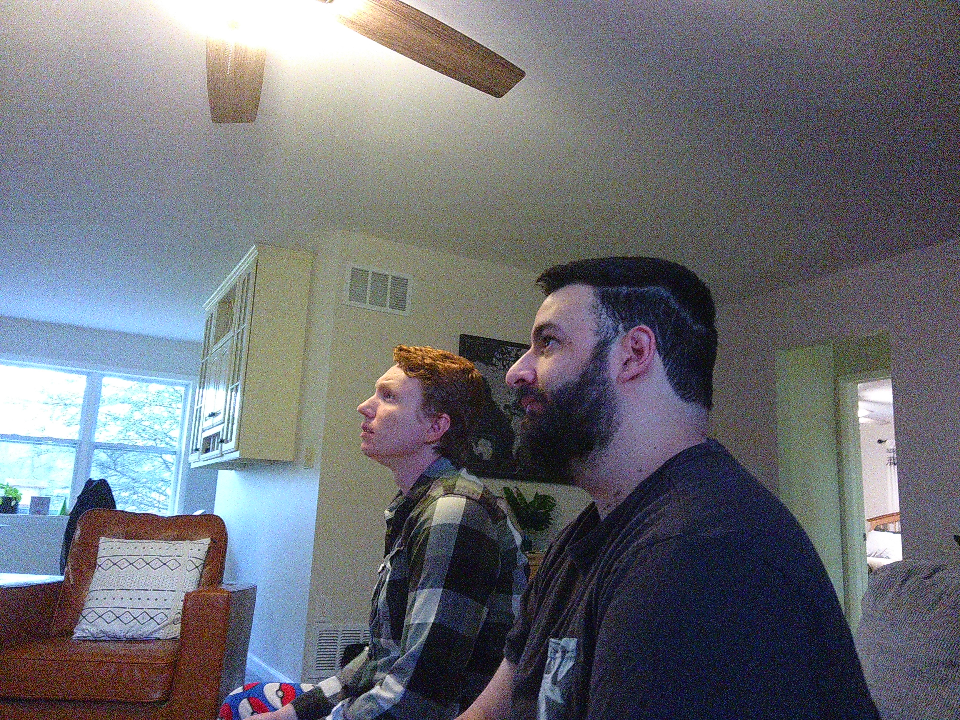 Picture of 2 men on a couch, looking off in the distance. They are playing some video game.