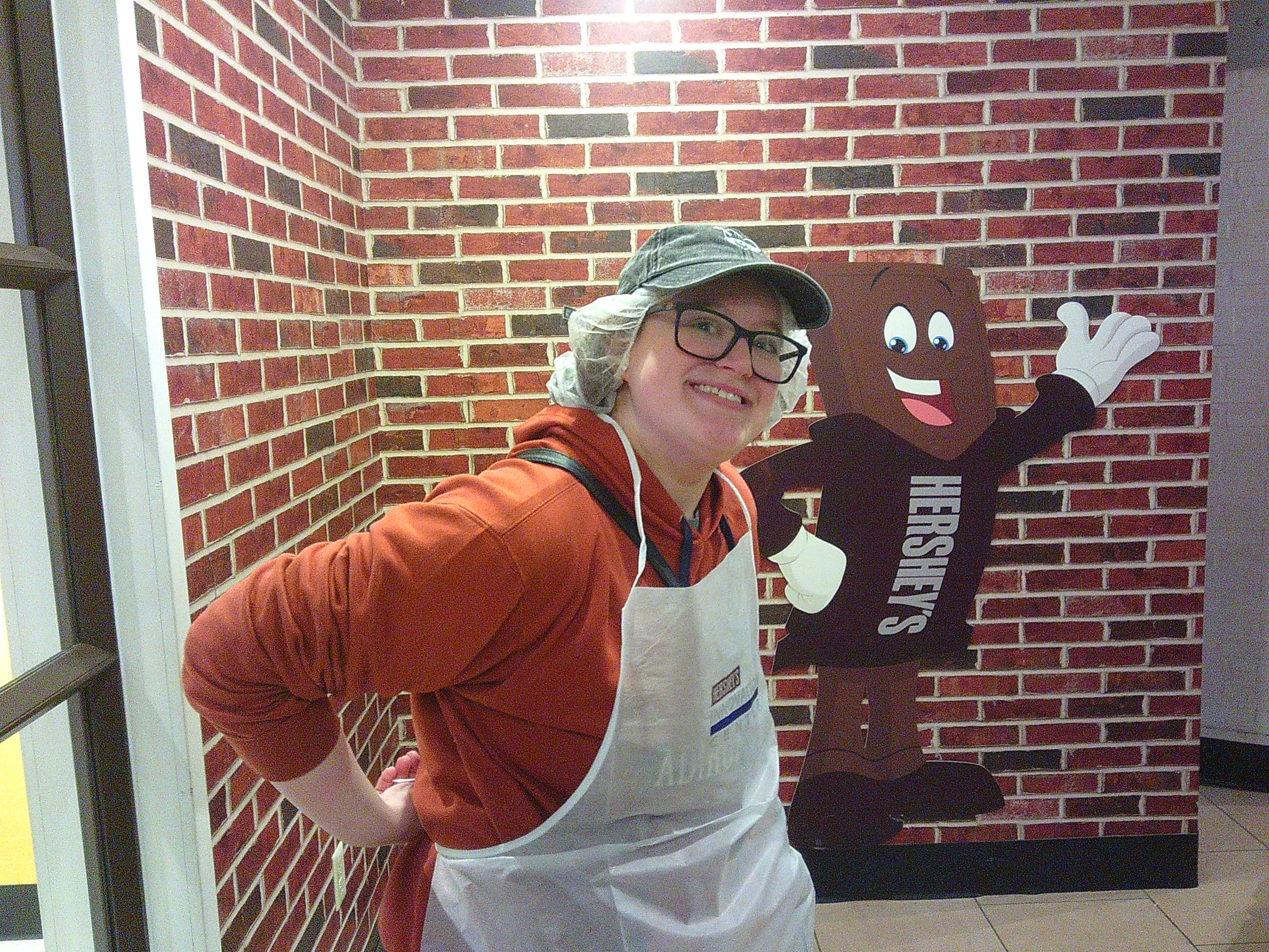 Picture of a woman putting on a white apron with a hairnet on smiling at the camera