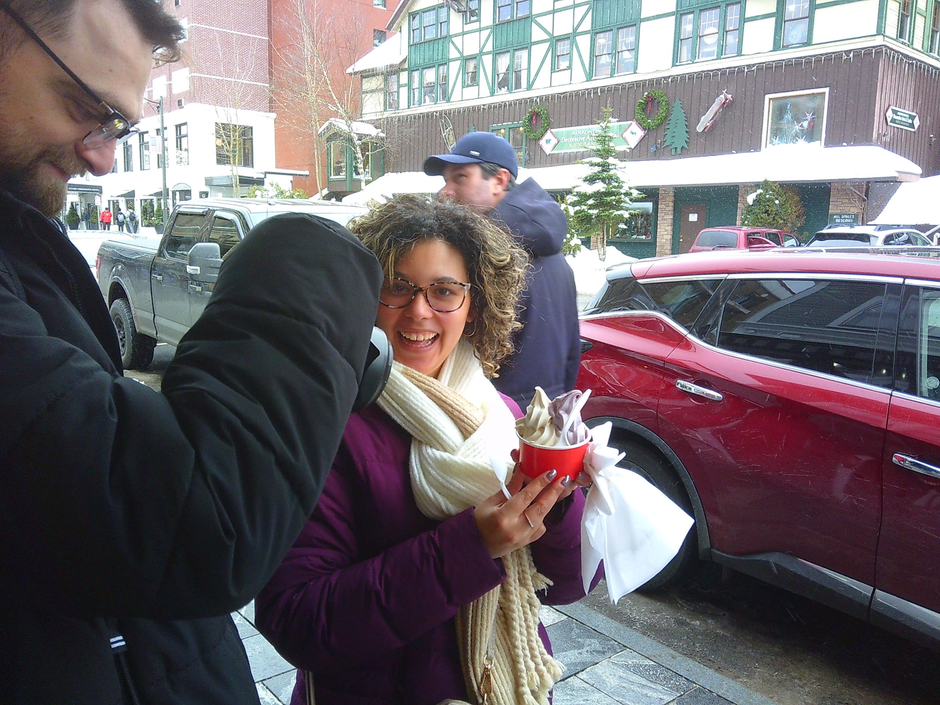 photo of Ali holding a cup of ice cream with white ice cream and purple ice cream in it. Tanner is trying to take a photo of the ice cream with his camera