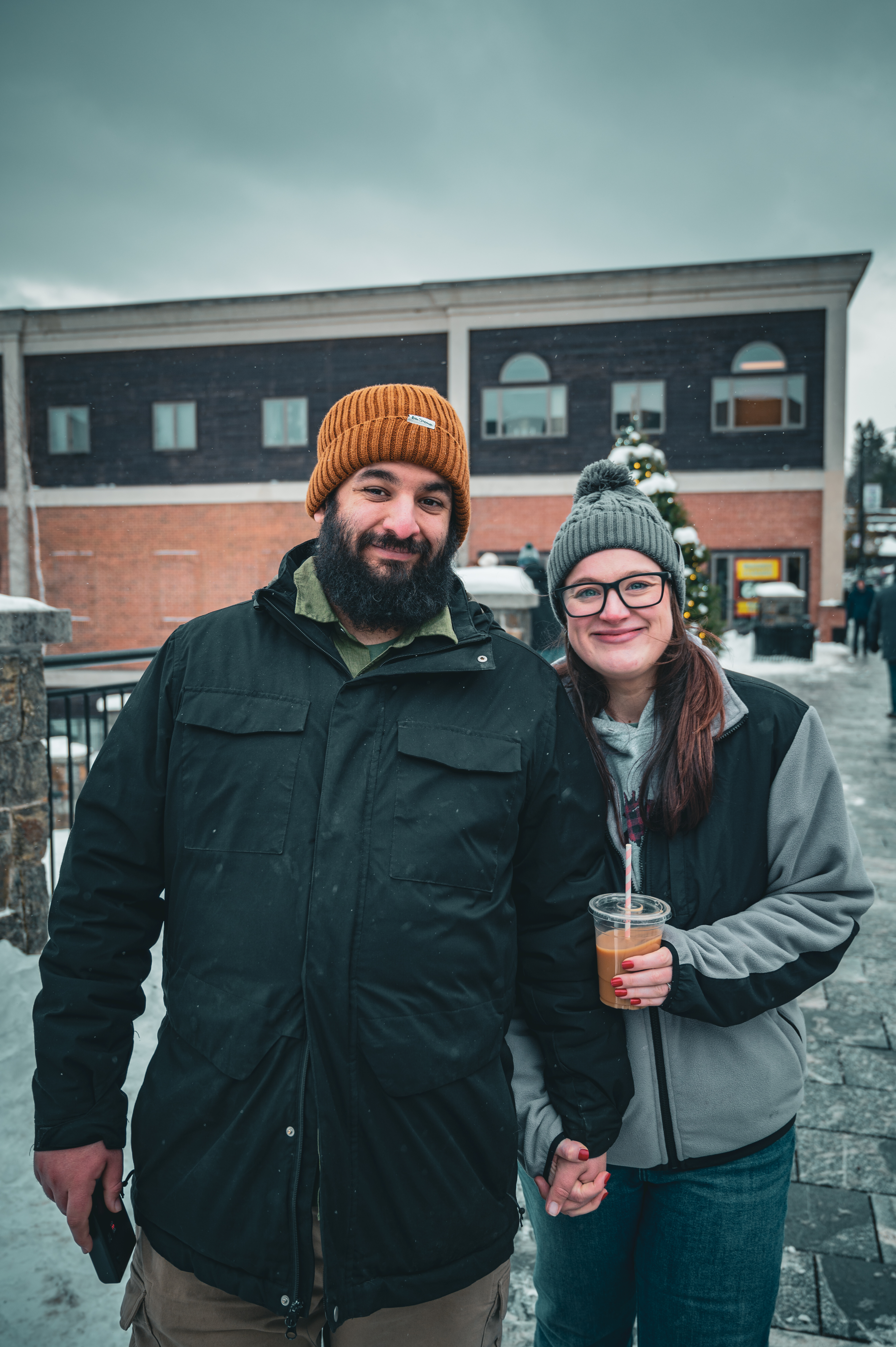 Portrait photo of Michelle and I holding hands, smiling at the camera, on a sidewalk. Michelle has a coffee in her hand, and I have my Camp Snap camera in my hand