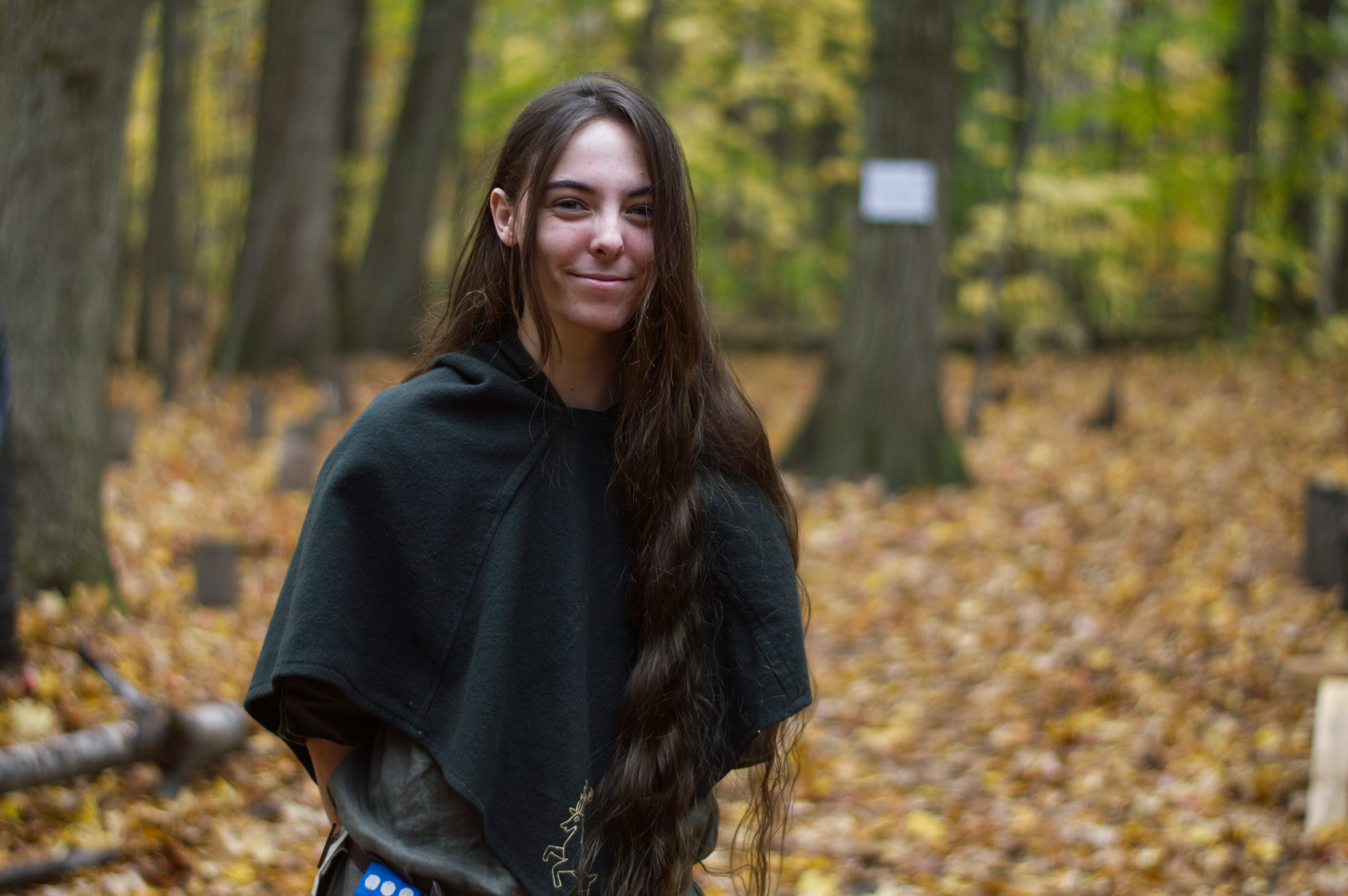 image of a person in the woods smiling. They have long hair, and are dressed like a medeival ranger.