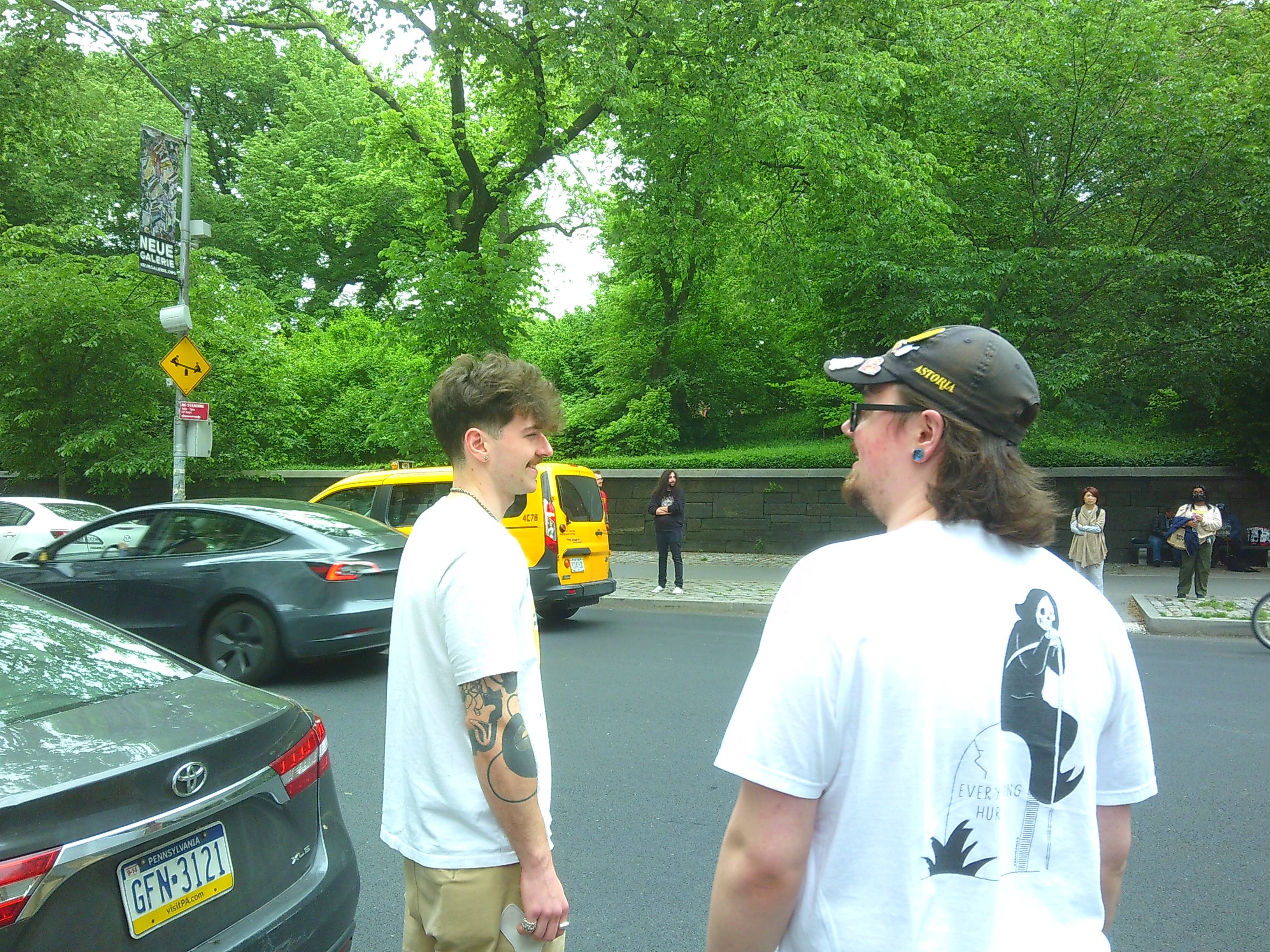 Two men (Skyler and Aiden from left to right) laughing while crossing a NYC street. A yellow taxi can be seen across the street, as well as a park