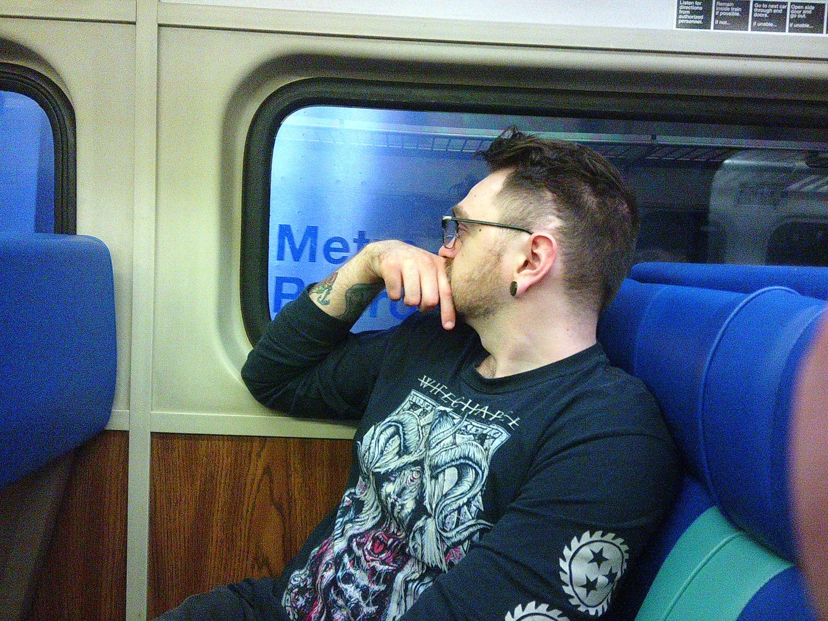 Picture of Tanner looking out of a train window to another passing train. The words 'Metro' can be roughly made out