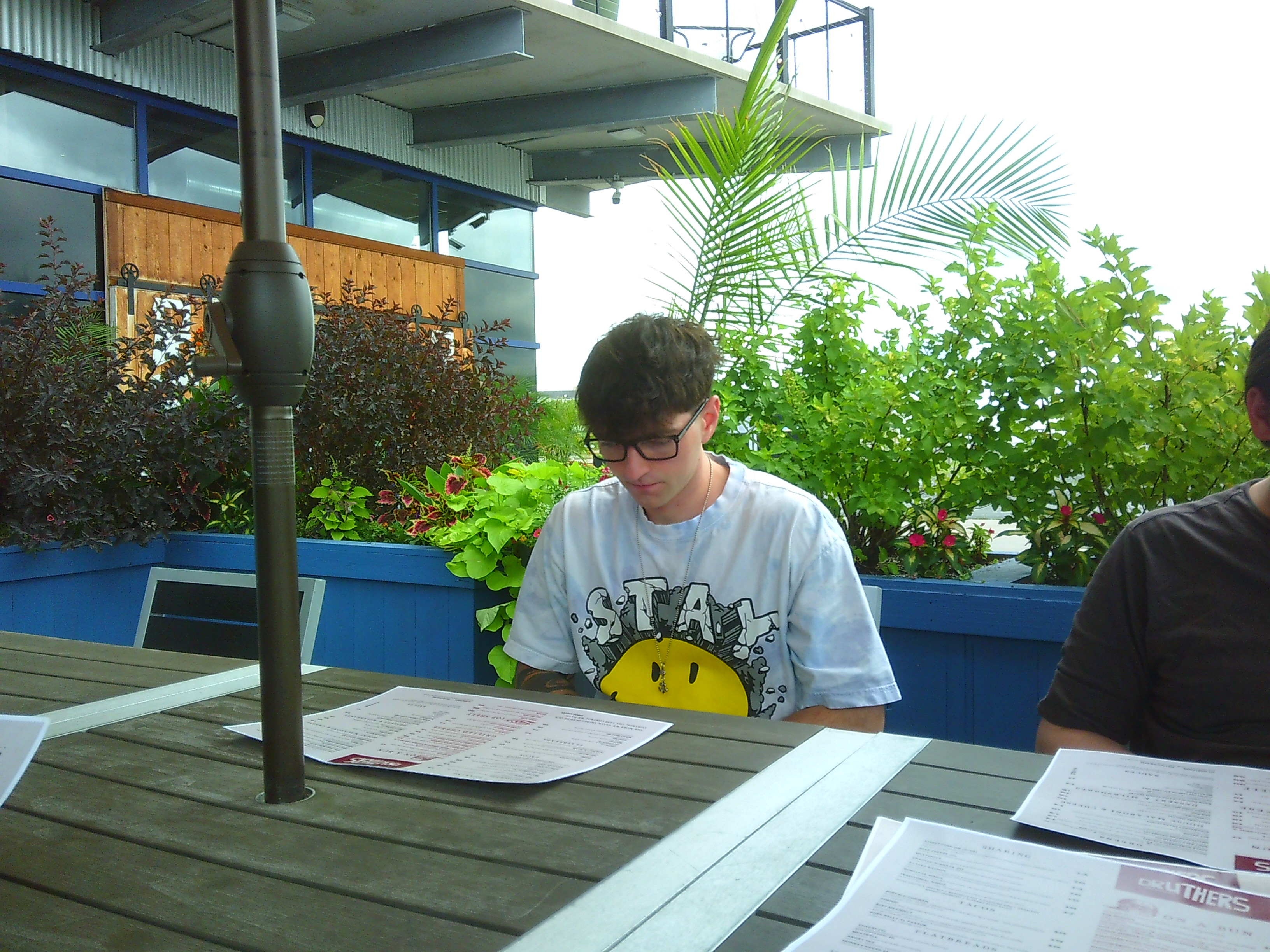 Photo of a man sitting outside at a restaurant table looking over a menu