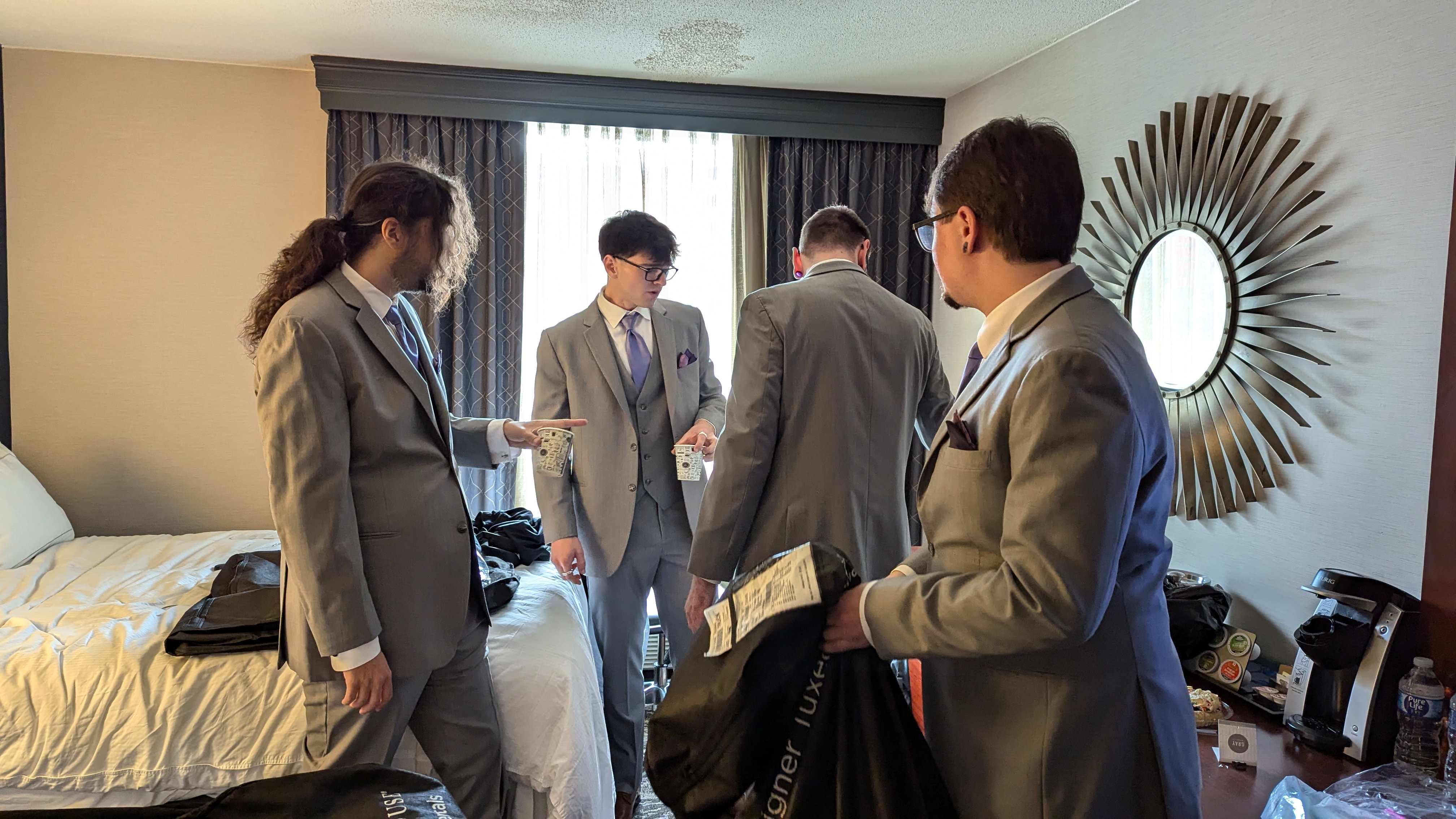 photo of four men in suits in a hotel room looking around for something