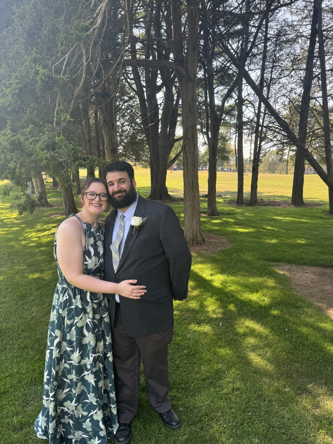 Photo of me and Michelle standing on a golf course in a nice suit and dress with our arms around each other smiling