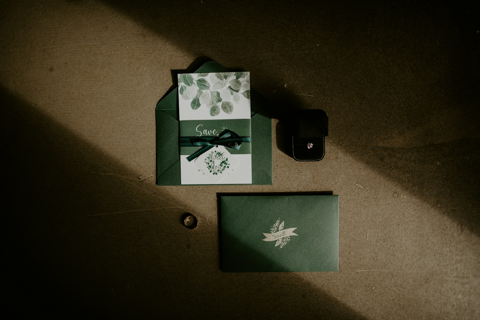 Photo of green envelopes and a card that says 'save' on it on a table. You can also see 2 rings on the table