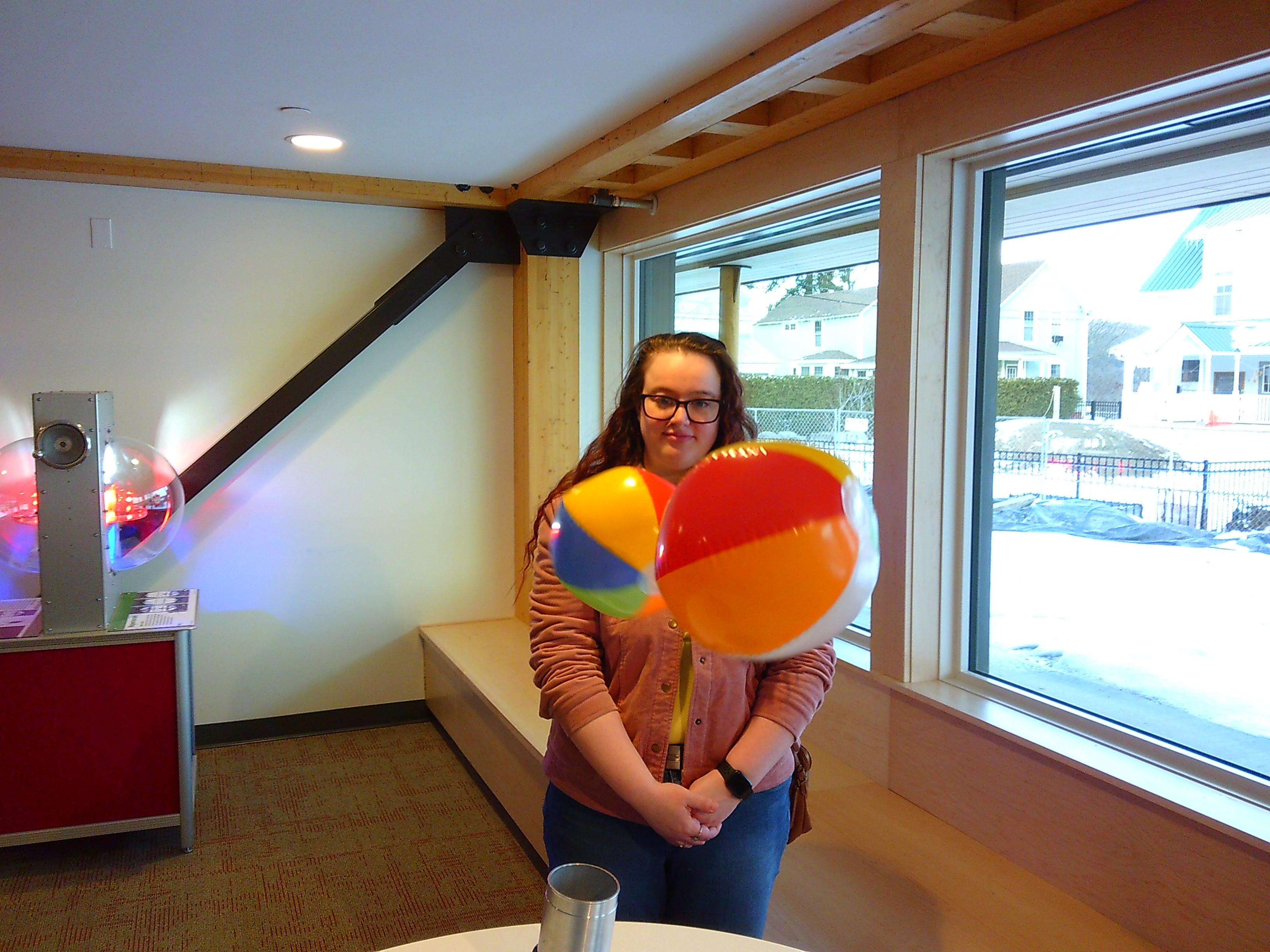 Inside shot of two multi-colored beach balloons floating in the air, with a woman staring at them from across a table