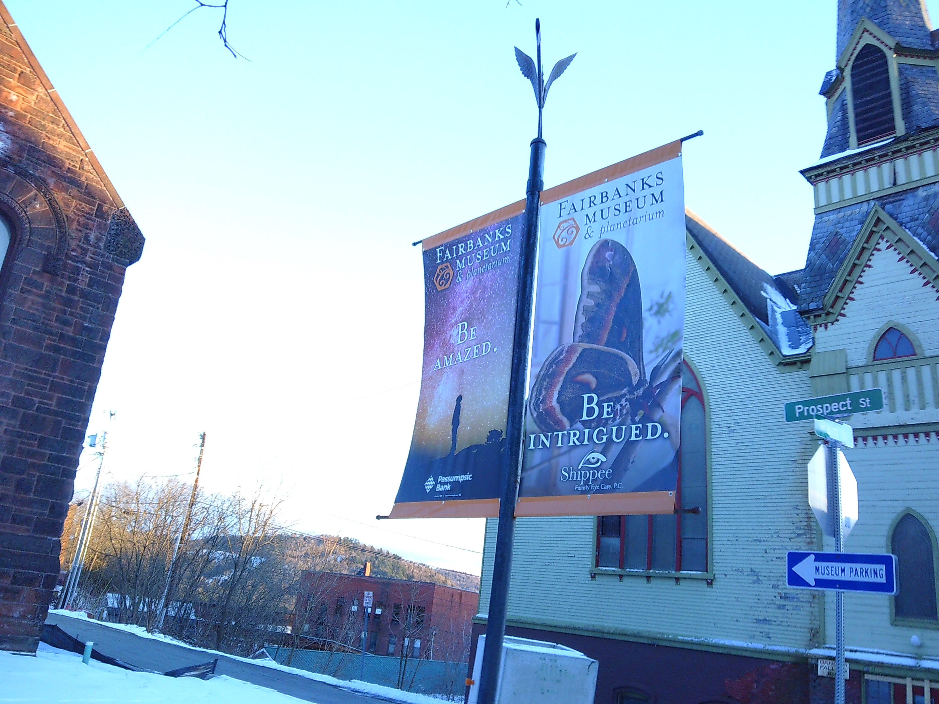 Outside shot of some signs that are promoting the Fairbanks Museum & Planetarium in St. Johnsbury Vermont. One says "Be Amazed" and shows the stars, the other says "Be Intrigued" and shows a butterfly