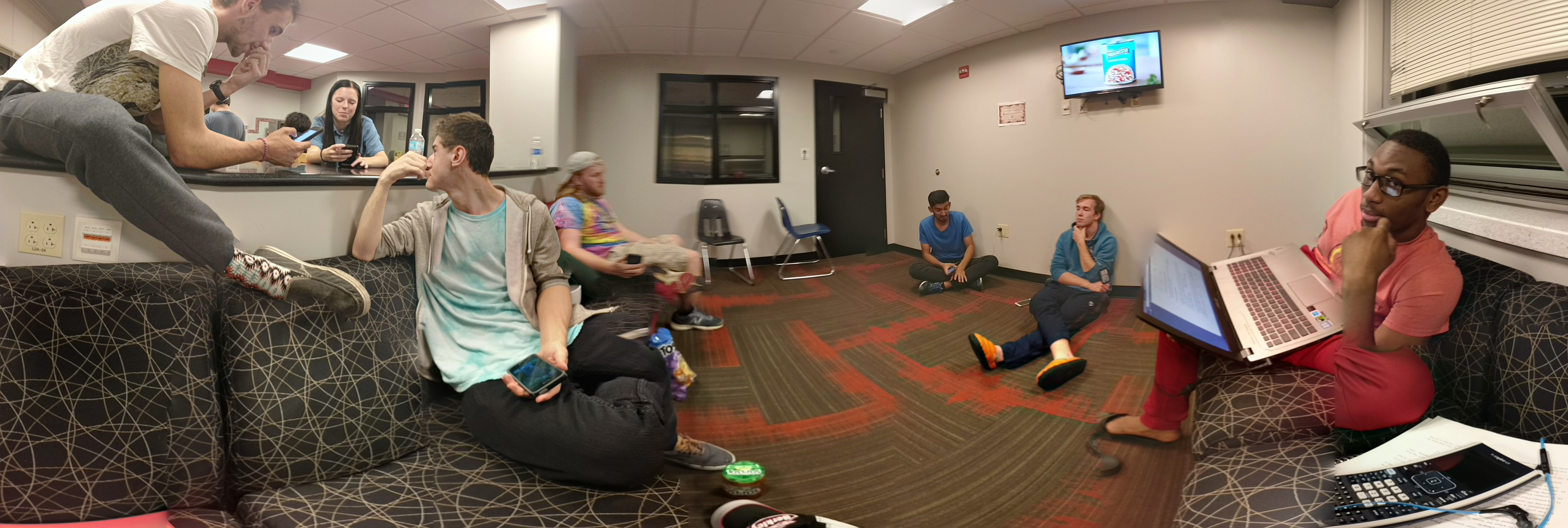 Photo of a group of people sitting on couches, on the floor, hanging out and talking with each other. We can see roughly 7 people